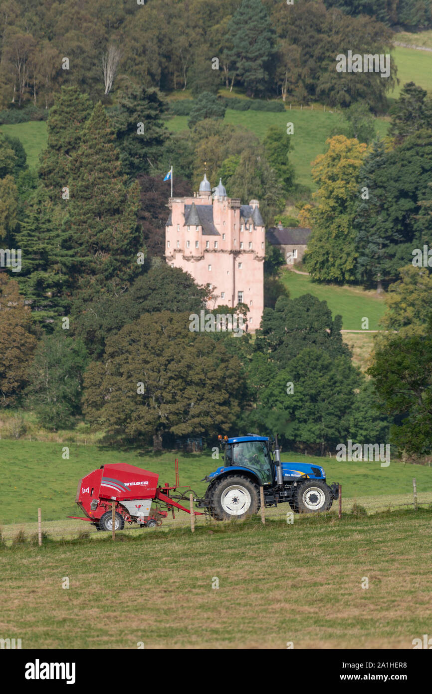 Une vue de l'Aberdeenshire campagne avec un agriculteur de la mise en balles de foin dans un champ en face de Craigievar Castle Banque D'Images