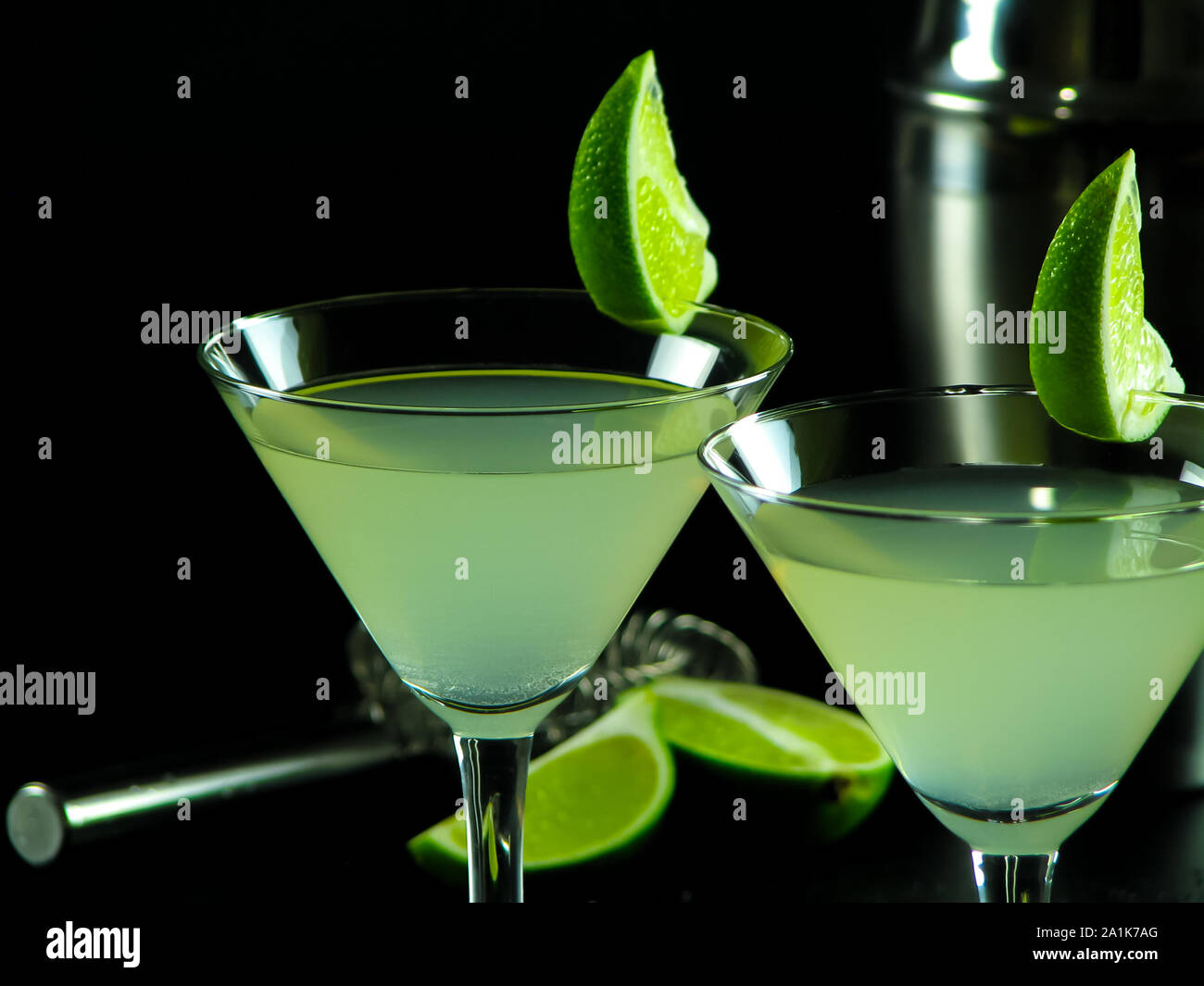 Cocktail sans alcool Daiquiri vert clair en verres à cocktail conique, décoré de tranches de citron vert, sur un fond sombre floue de shaker, tamis Banque D'Images