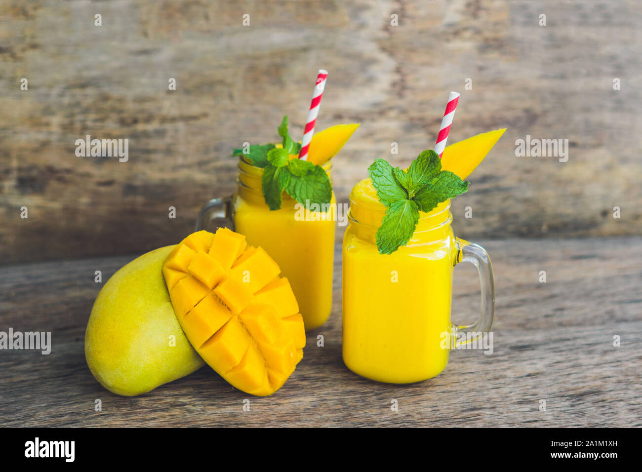 Smoothie juteux à la mangue dans deux pots en verre de maçon avec paille rouge rayée sur fond de bois ancien. Concept de vie saine, espace de copie Banque D'Images