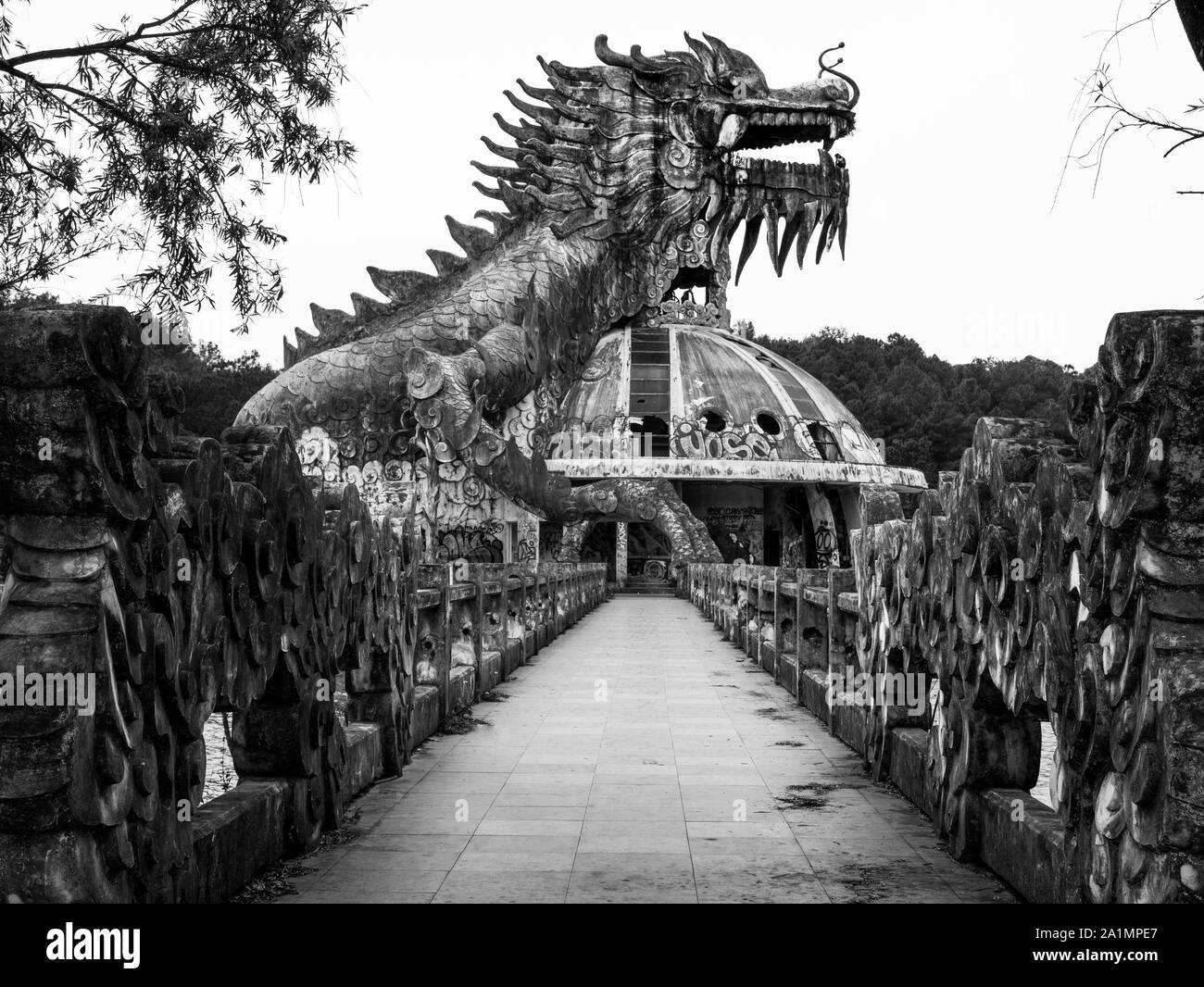 Immense et effrayant dragon en pierre de pointes et bouche ouverte avec dents en vue de profil avec sentier abandonné au parc de l'eau, noir et blanc, Hue, Vietnam Banque D'Images