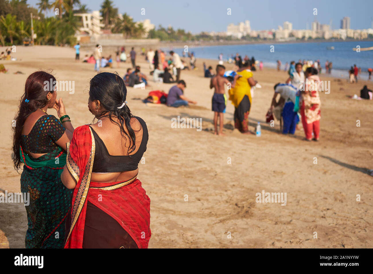 Deux femmes indiennes vêtues de sari-d'oeil sur la plage de Chowpatty, Mumbai, Inde, baigné de lumière de l'après-midi chaud et avec de nombreux autres visiteurs dans la b/g Banque D'Images