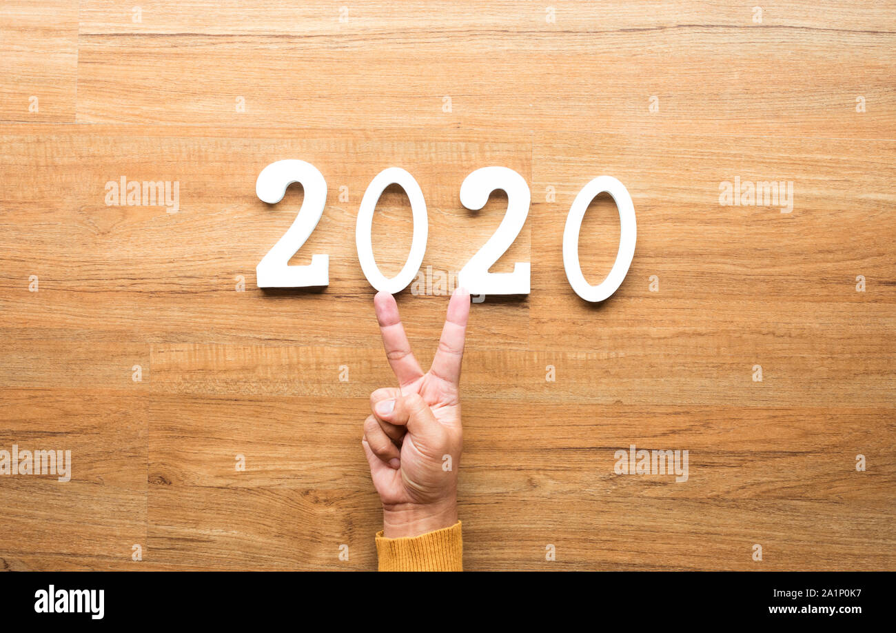 2020 Nouvel an fête concepts avec texte numéro et main humaine montrant V signe sur fond de bois. d'inspiration et de motivation idées Banque D'Images