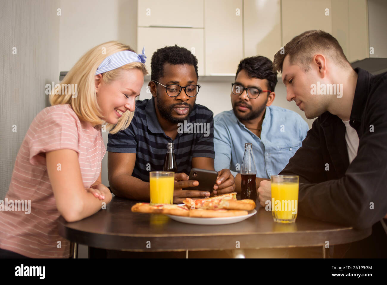 Quatre amis assis à table, de manger des pizzas, boivent des boissons alcoolisées, la lecture de message texte sur smartphone, l'essai de nouvelles application téléphone ensemble. Mult Banque D'Images