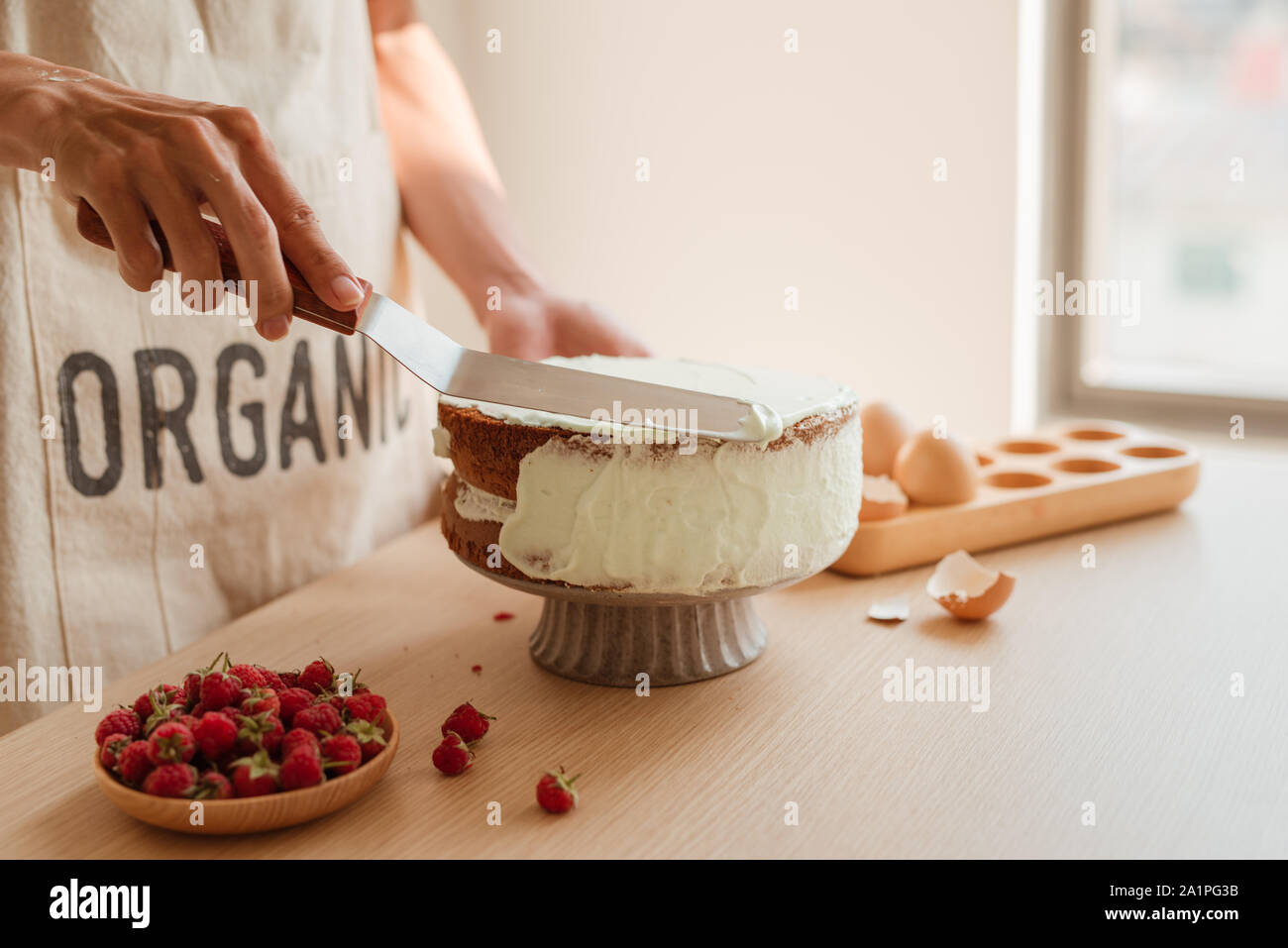 La main de l'homme mettre la crème fouettée sur le gâteau éponge. Gâteau éponge en série. Banque D'Images