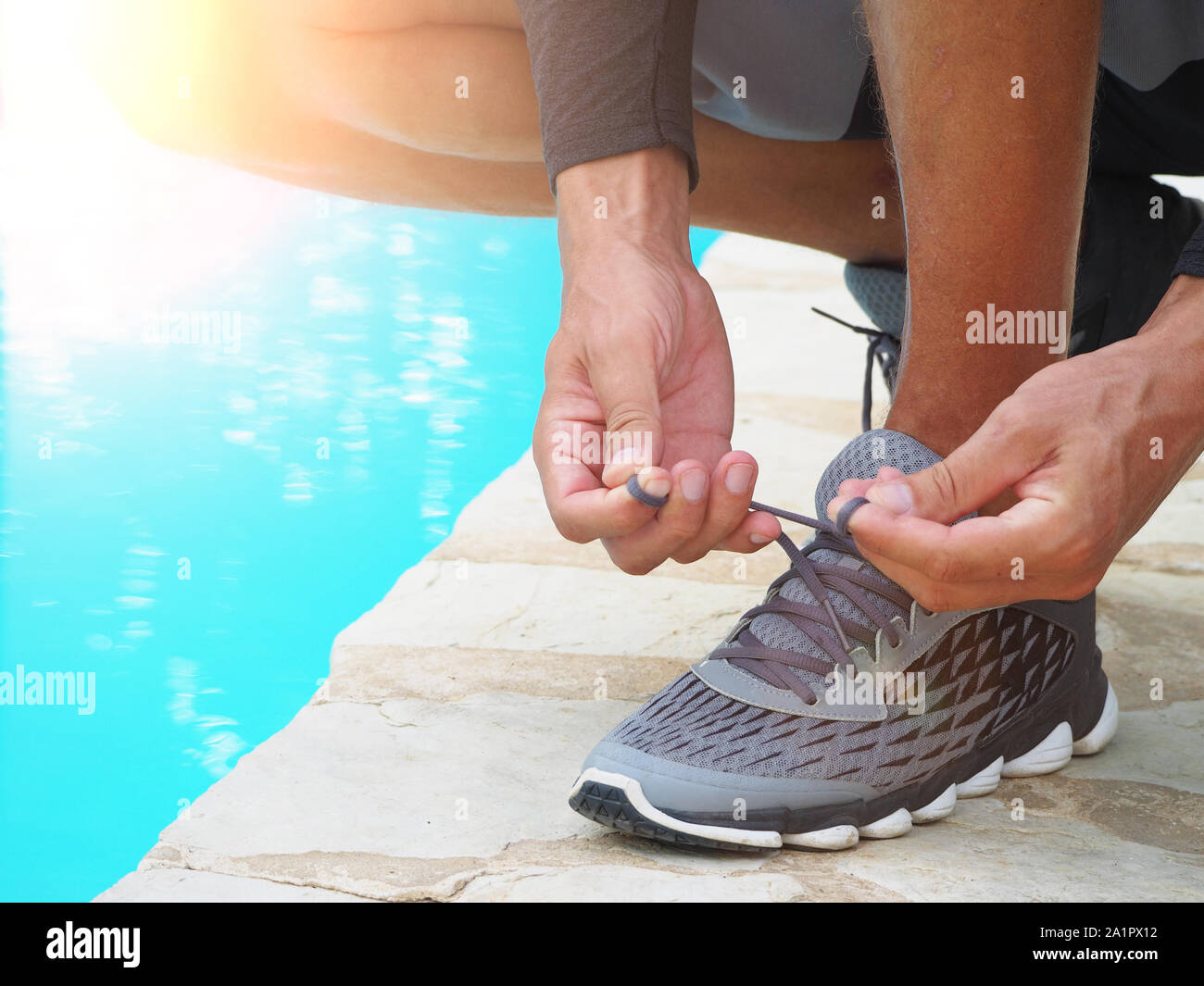 L'image d'un homme attacher ses lacets de sneakers près d'une piscine. Banque D'Images
