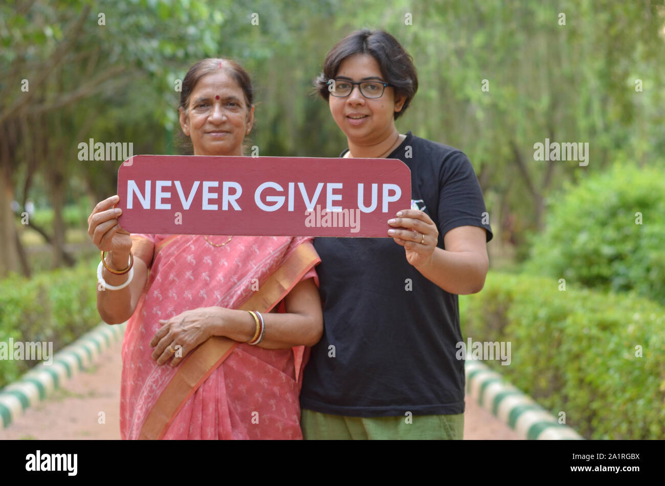 Bengali Senior femme indienne avec sa jeune fille tenant une pancarte avec le message "ne jamais abandonner" dans un parc à New Delhi, Inde Banque D'Images