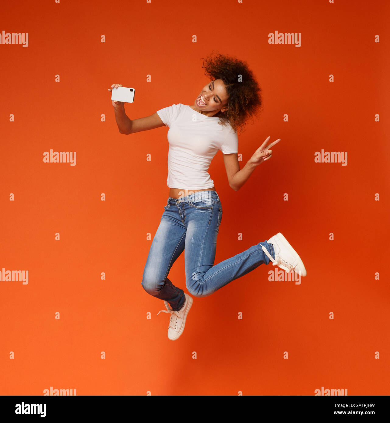 Cute african american girl jumping et décisions sur smartphone selfies Banque D'Images