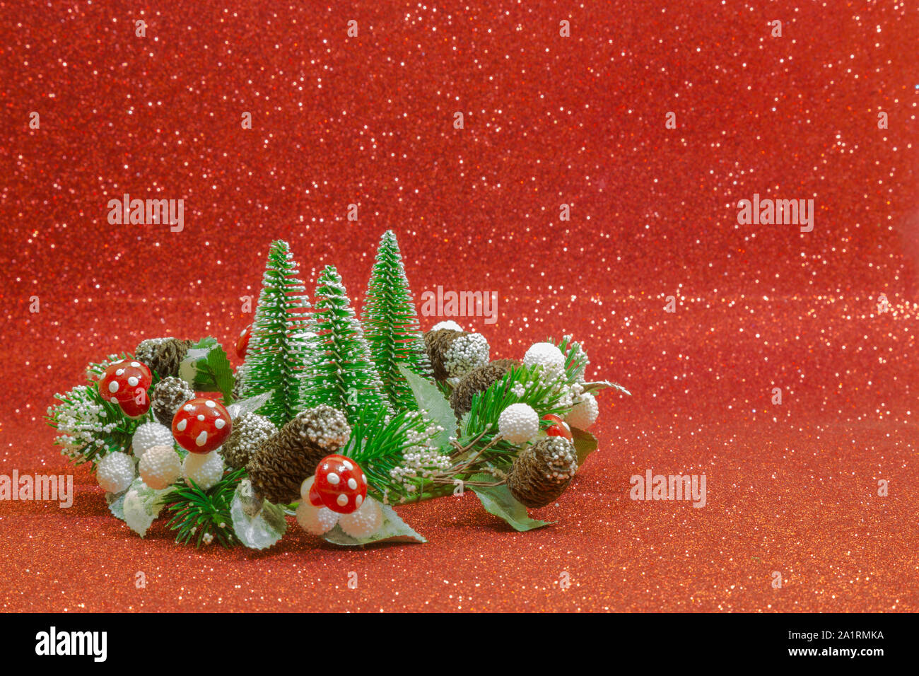 Trois arbres de Noël et une guirlande décorée avec des champignons rouges, boules blanches et de petites pommes de pin sur un fond rouge. Banque D'Images