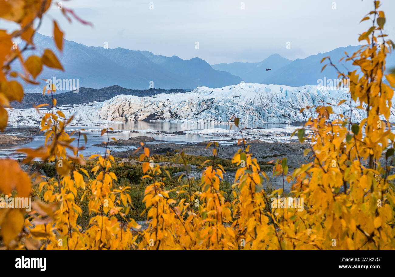 Un petit avion de brousse vole bas au-dessus de la cascade de la Matanuska Glacier en Alaska. Un peu de lumière à travers les nuages et la fumée des pics juste avant le coucher du soleil, fr Banque D'Images