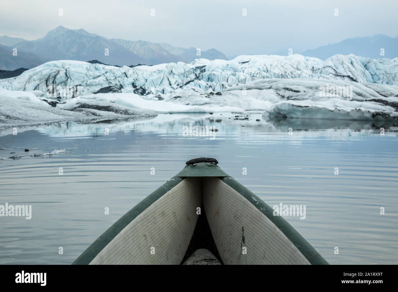 La fumée remplit le ciel au-dessus du glacier Matanuska, comme un canoë gonflable est pagayé entre les icebergs en dessous du glacier. Banque D'Images