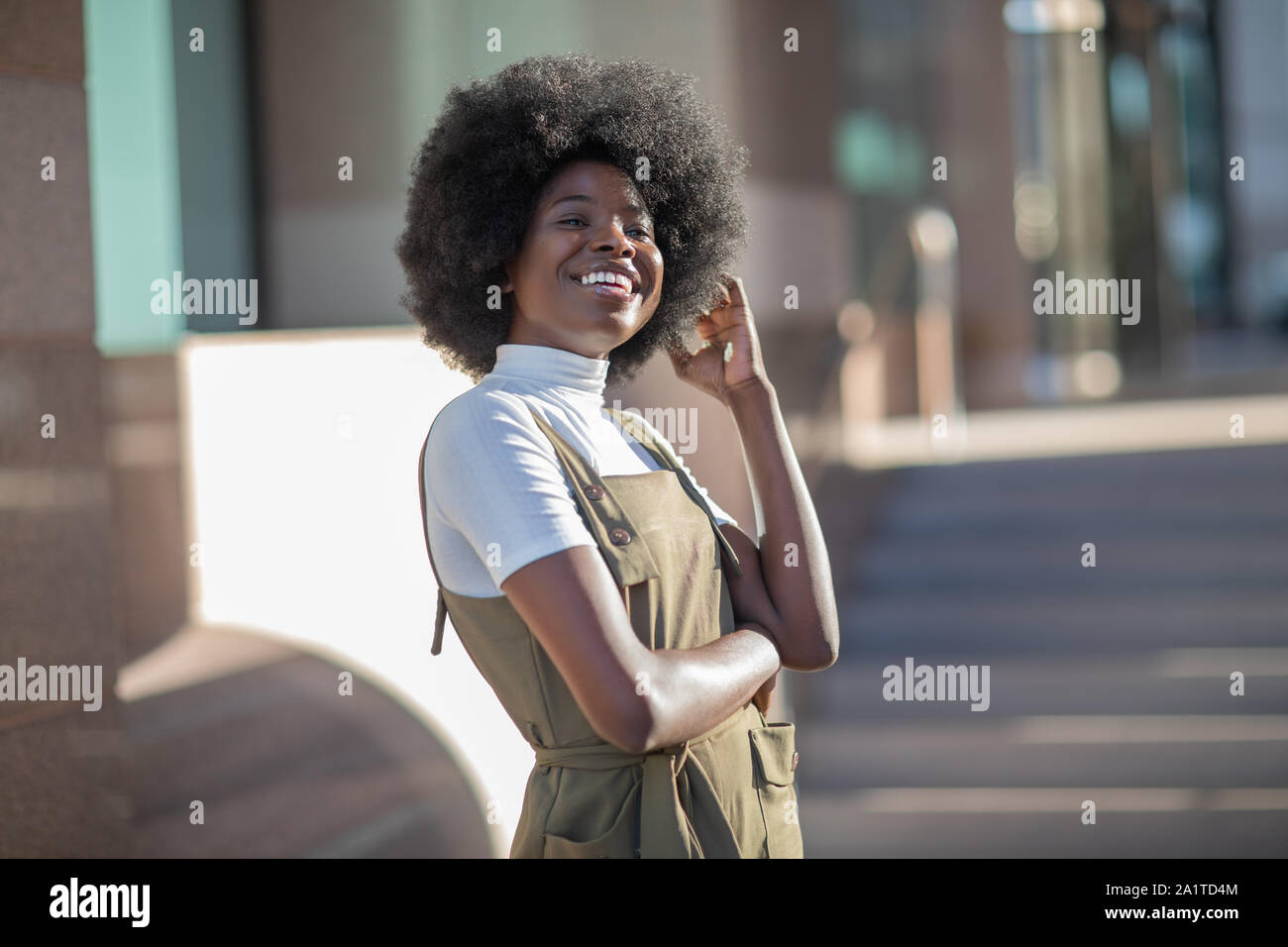Belle African American girl avec un sourire et des cheveux bouclés, la mode des bretelles, et col roulé blanc. Banque D'Images