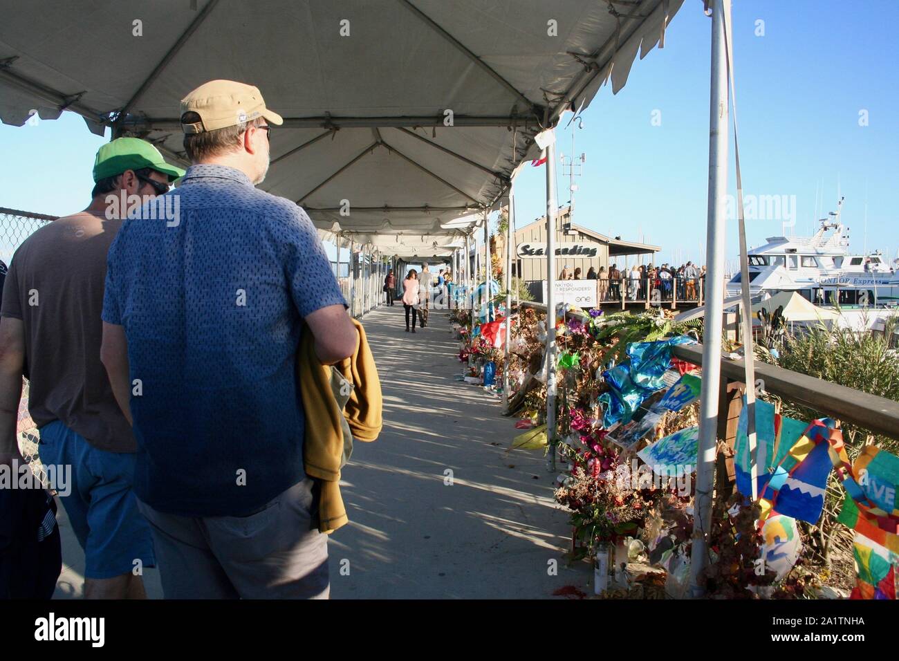 Santa Barbara, Californie, USA. 28 Sep, 2019. Mémorial pour bateau de plongée victimes perdues en mer continue d'aller en mer forte quai de débarquement, dans le port de Santa Barbara, où la conception était le refuge avant la fête du Travail accident qui a tué 34 personnes sur une période de trois jours de vacances aux îles Anglo-Normandes. Un navire de croisière compagnie vient de mettre en place un auvent et de clôture, et les touristes sont curieux et respectueux comme ils marchent par le mémorial. Photos de ceux qui ont perdu leur vie est entourée de fleurs, de nombreux secs maintenant, mais avec une douce's encore déposées tous les jours. Chaque soir, les bougies sont allumées Banque D'Images