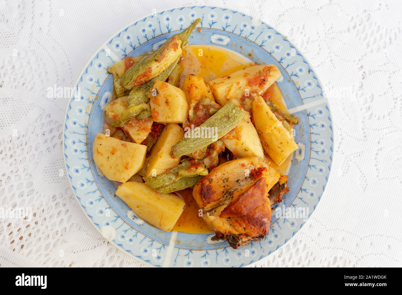 Une authentique Assiette de poulet au four crétois avec des pommes de terre et courgettes (zuccini) dans une riche sauce tomate et sauce d'huile d'olive aux herbes Banque D'Images