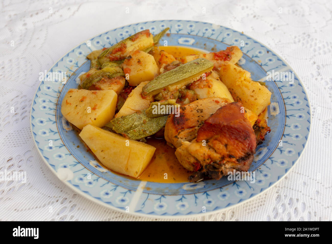 Une authentique Assiette de poulet au four crétois avec des pommes de terre et courgettes (zuccini) dans une riche sauce tomate et sauce d'huile d'olive aux herbes Banque D'Images