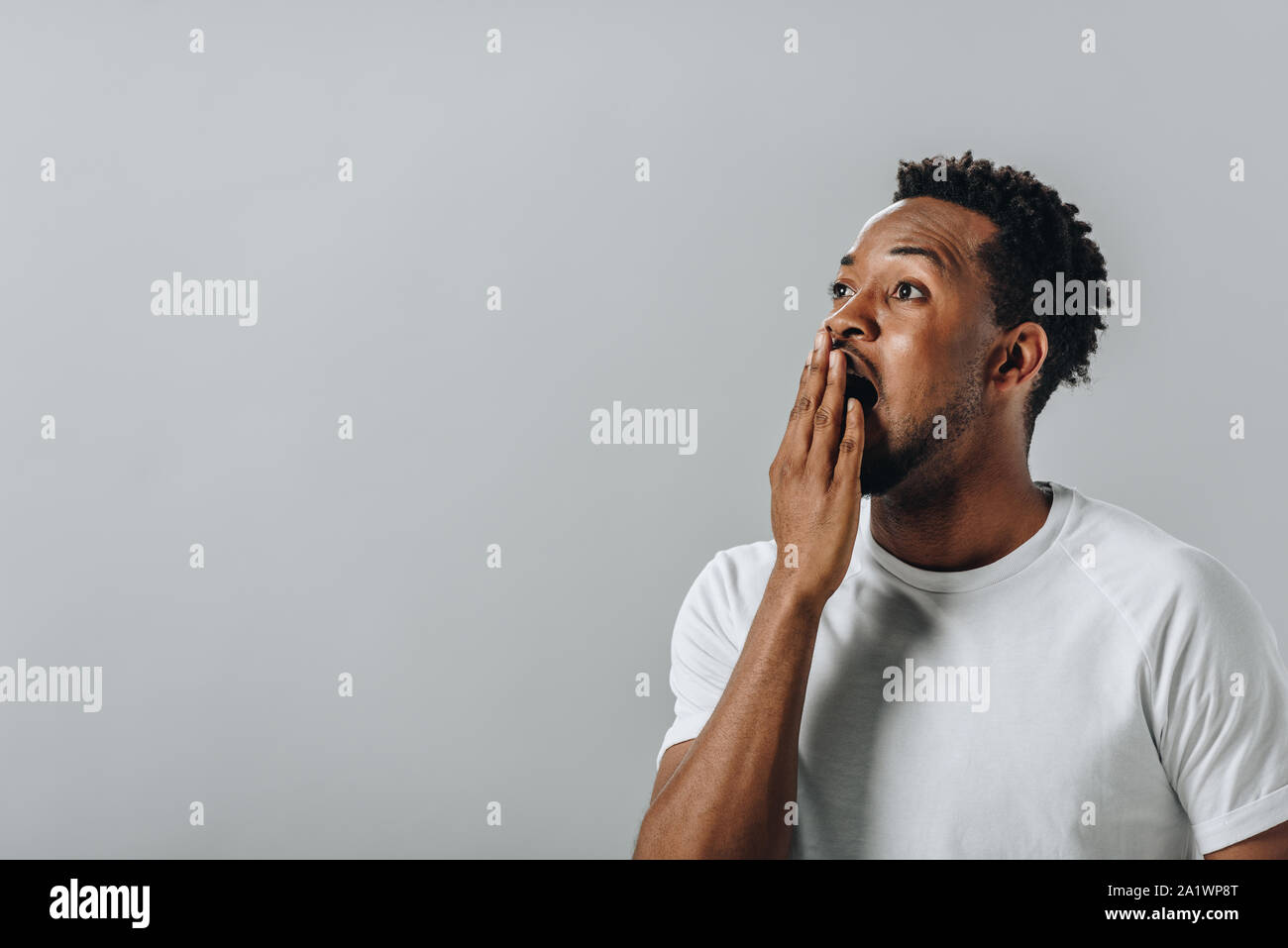 Choqué African American man in white T-short couvrant la bouche avec la main et à la caméra à l'isolé sur gray Banque D'Images