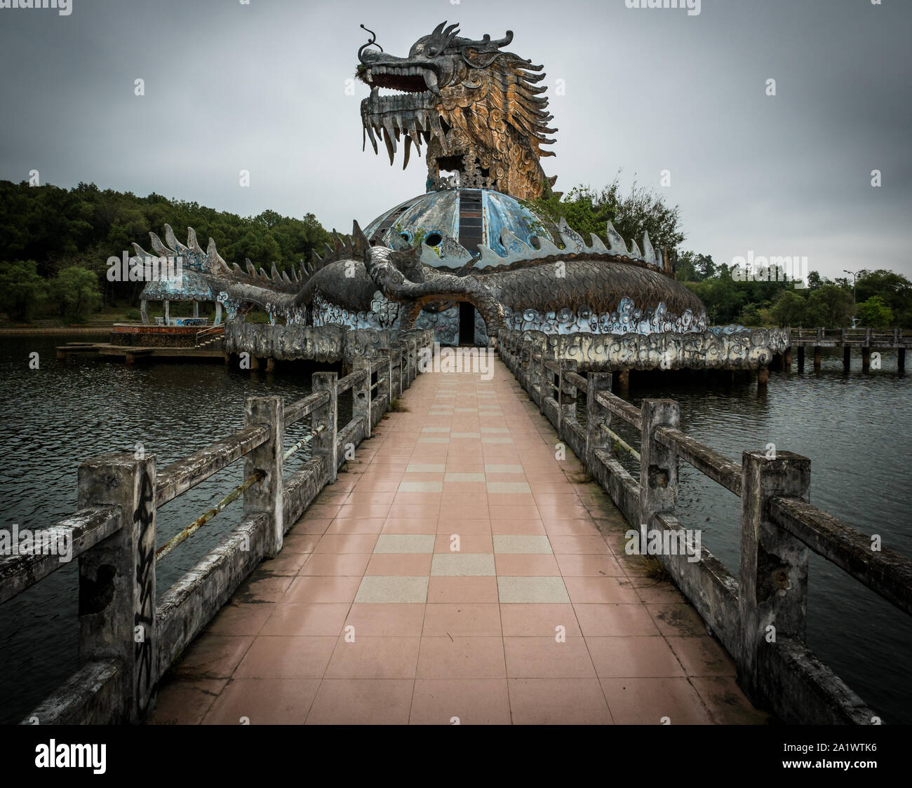 Immense et effrayant dragon en pierre de pointes et bouche ouverte avec dents en vue de profil avec sentier au parc aquatique abandonné, Thuy Tien lake, Hue, Vietnam Banque D'Images