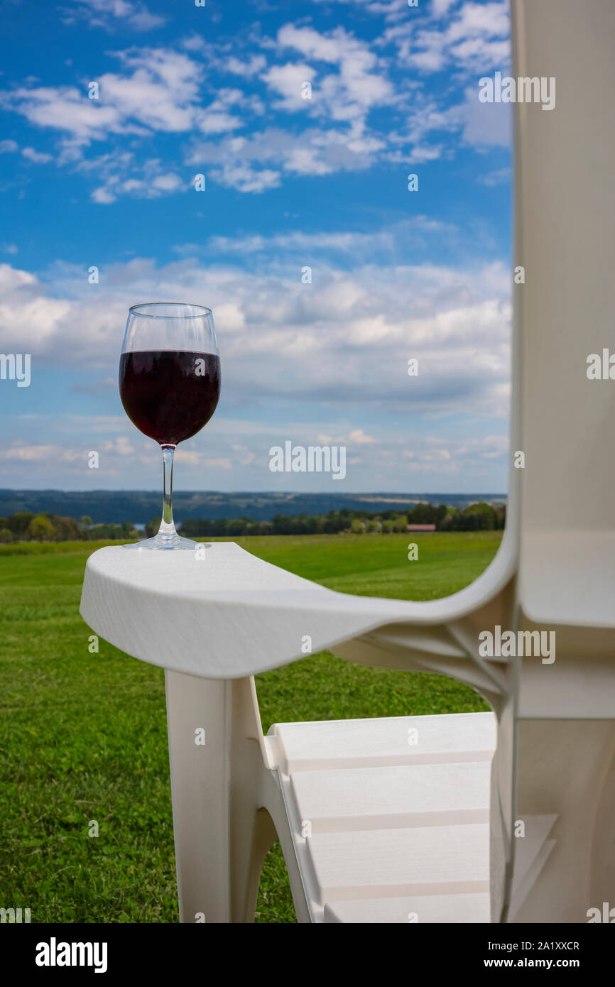 Un verre de vin rouge a photographié à sur l'accoudoir d'une chaise Adirondack en plastique blanc, près de Cayuga Lake dans la région des lacs Finger de l'État de New York Banque D'Images