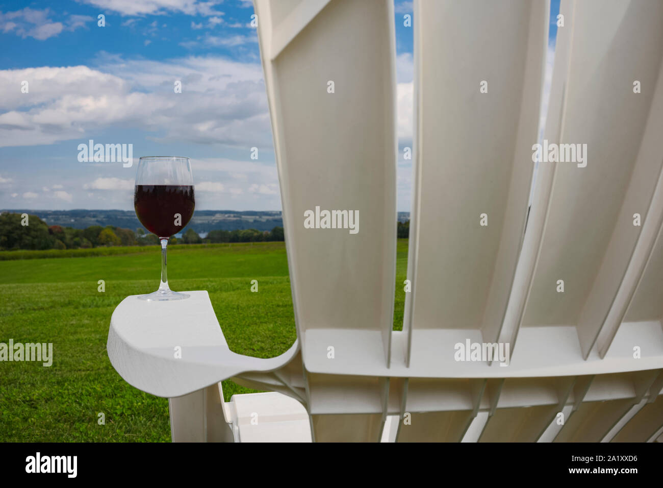 Un verre de vin rouge a photographié à sur l'accoudoir d'une chaise Adirondack en plastique blanc, près de Cayuga Lake dans la région des lacs Finger de l'État de New York Banque D'Images