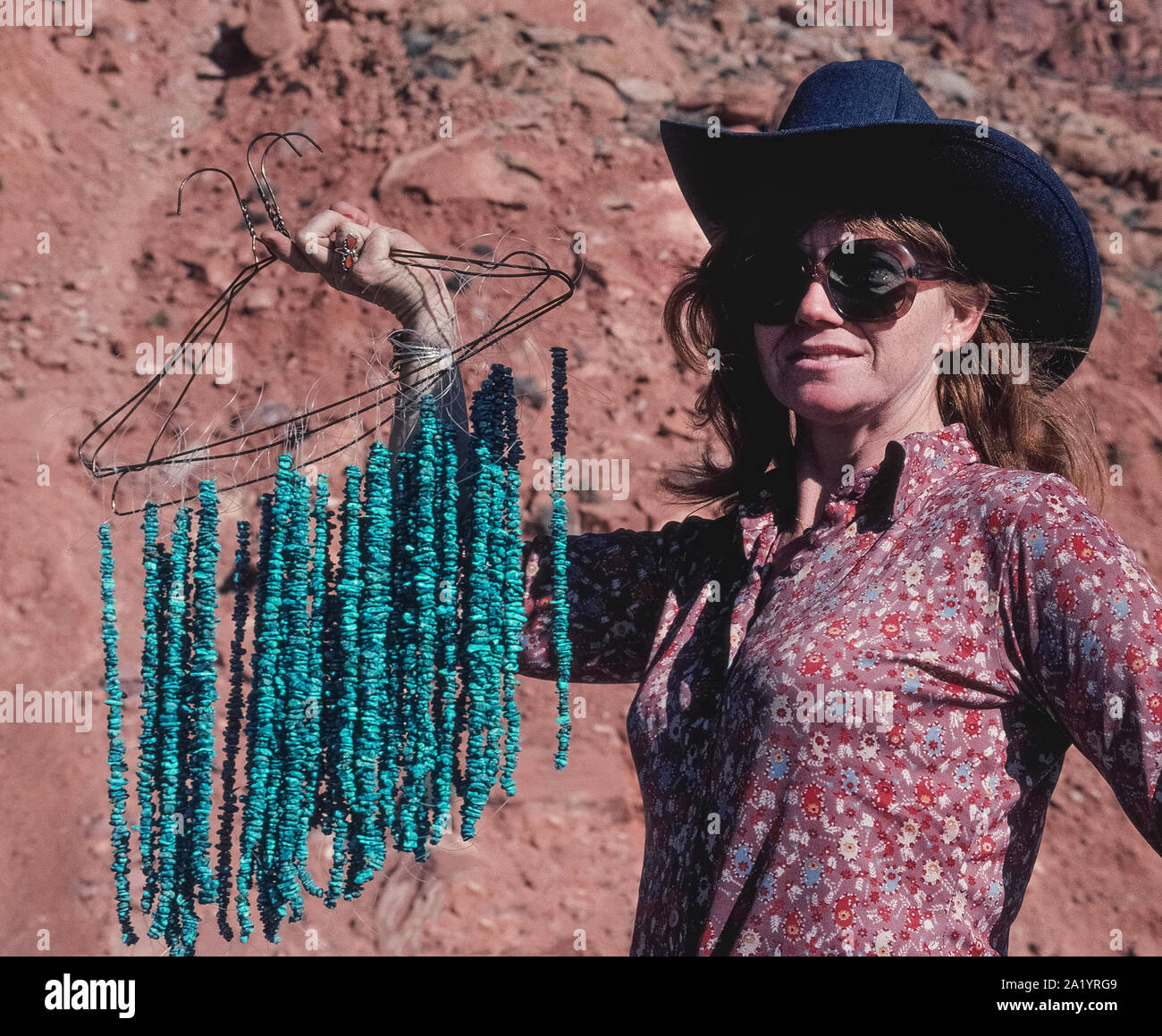 Une femme portant un chapeau de cowboy et de grandes lunettes de soleil contient jusqu'cintres de fil pour afficher des chaînes de petites billes de turquoise, elle vend aux touristes qui s'arrêtent le long d'une route dans le sud-ouest de l'Arizona, USA. L'opaque, bleu-à-vert pierre semi-officielle de l'Etat a été désigné le joyau de l'Arizona en 1974. Les Indiens Navajo et d'autres Amérindiens de la sud-ouest des États-Unis sont célèbres pour l'aide à créer des bijoux turquoise unique et à la mode, les articles qui vont de colliers, bracelets et boucles d'oreilles pour bracelets et boucles de ceinture. Banque D'Images