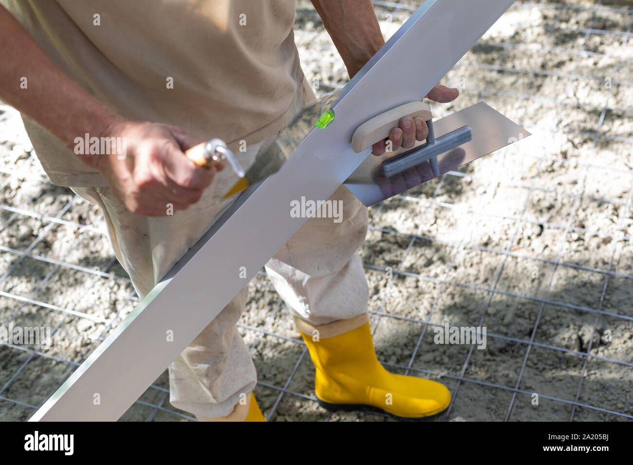 Travailleur de la construction en bottes de caoutchouc jaune sur le site de construction, lisser et lisser le béton Banque D'Images