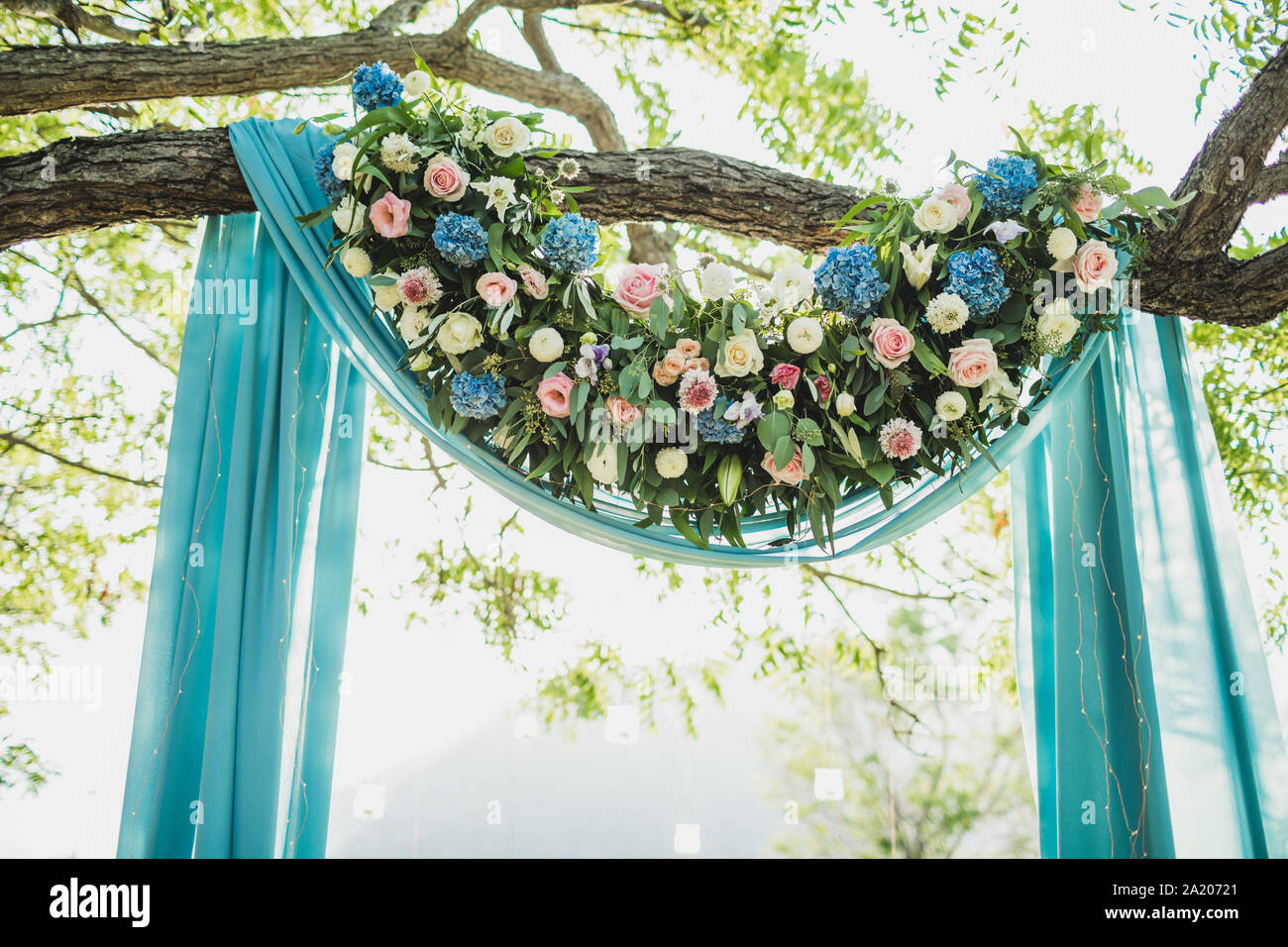 Cérémonie de mariage Sunset arch avec décoration de fleurs et tissu bleu accroché sur la canopée grand arbre. Hortensia bleu, rose, Lily. De couleur pastel. Banque D'Images