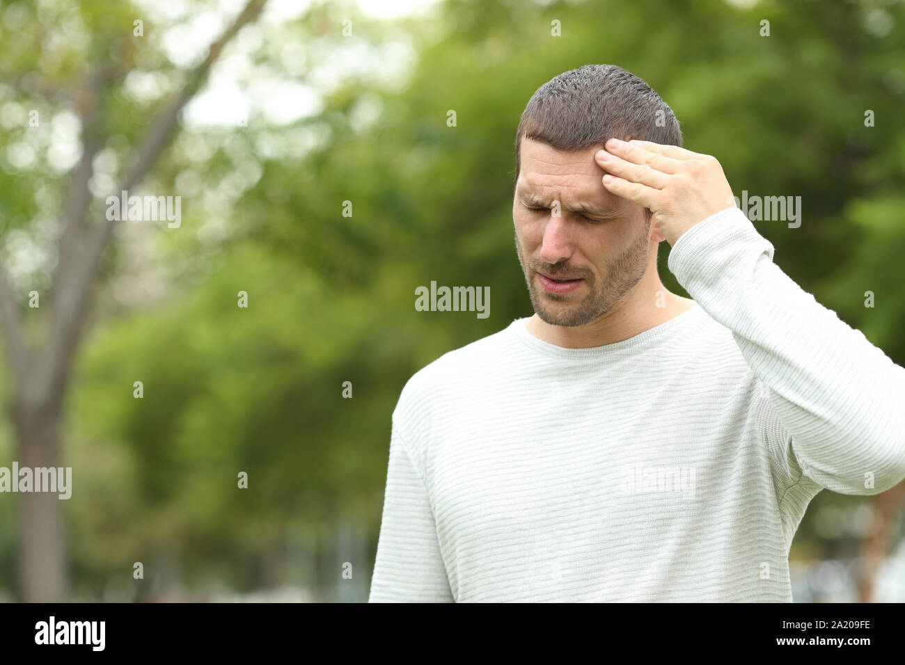 La souffrance de l'homme seul debout tête ache se plaindre dans un parc aux arbres verts dans l'arrière-plan Banque D'Images