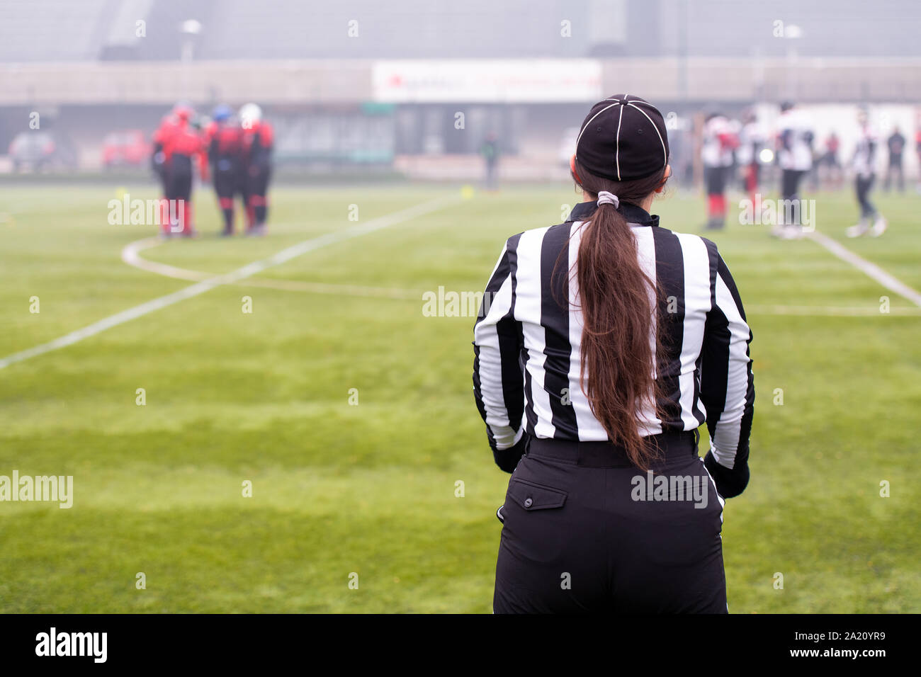 Vue arrière de l'arbitre de football américain féminin signaux donnant aux joueurs professionnels au cours de match sur le terrain du stade Banque D'Images