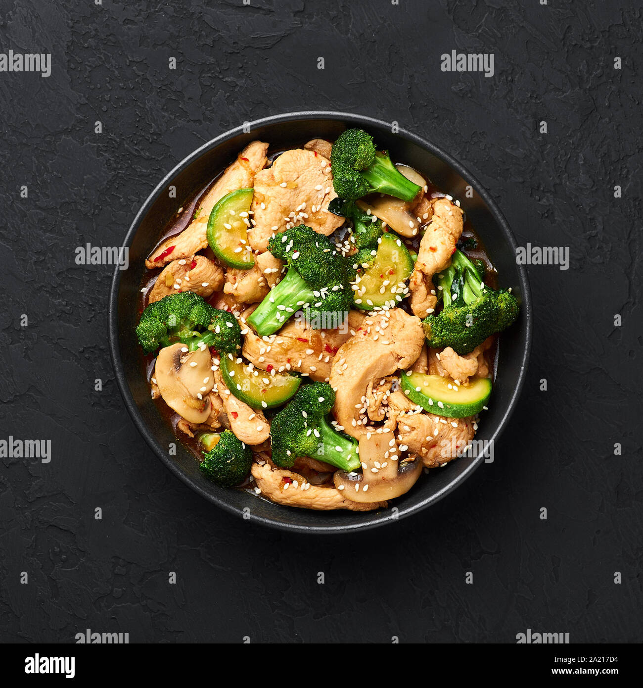 Poulet au Hunan bol noir dark slate à fond. Poulet Hunan est chinois ou l'indo-chinoise plat à emporter avec brocoli, courgettes, shiitake Banque D'Images