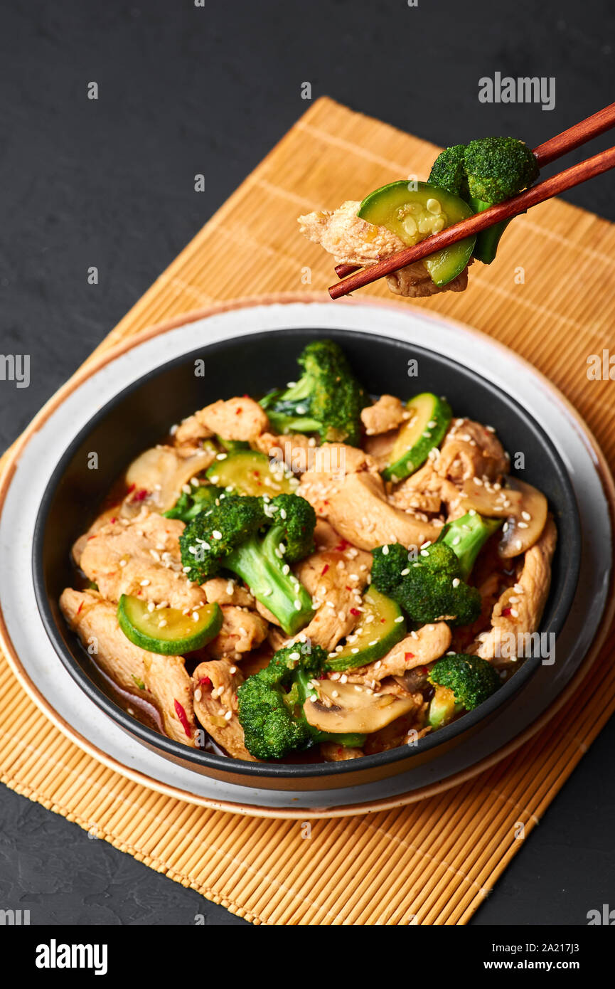 Poulet au Hunan bol noir dark slate à fond. Poulet Hunan est chinois ou l'indo-chinoise plat à emporter avec brocoli, courgettes, shiitake Banque D'Images