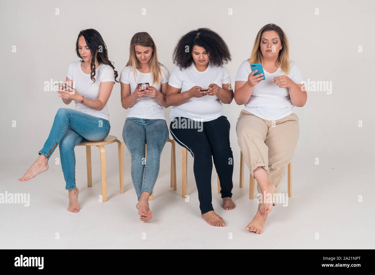 Groupe des belles filles assis sur des chaises et à l'aide de smartphones sur fond blanc. Les gens et les gadgets modernes Banque D'Images