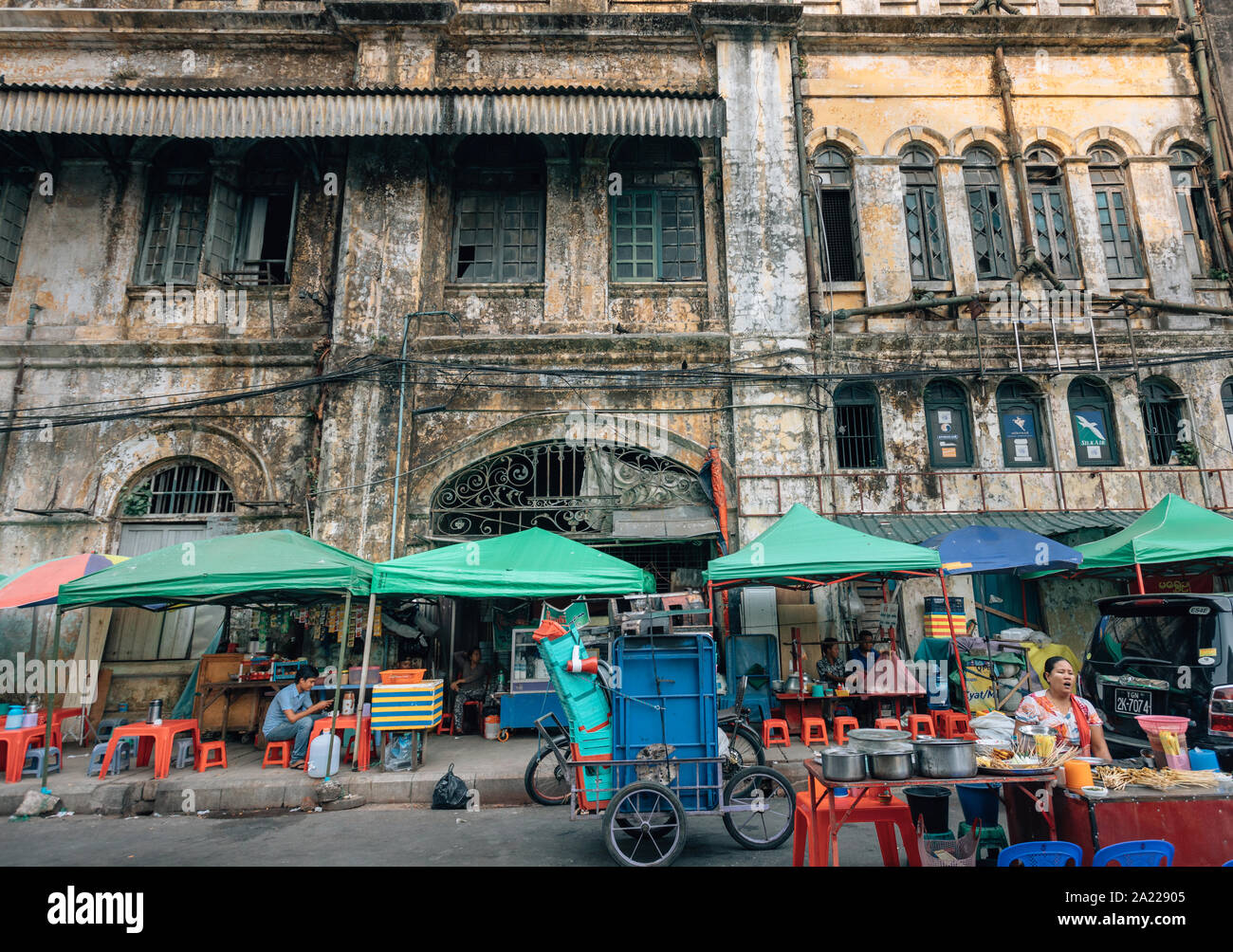Yangon, Myanmar - vendeurs d'aliments de rue devant un vieux bâtiment en ruines à Yangon, Birmanie Banque D'Images