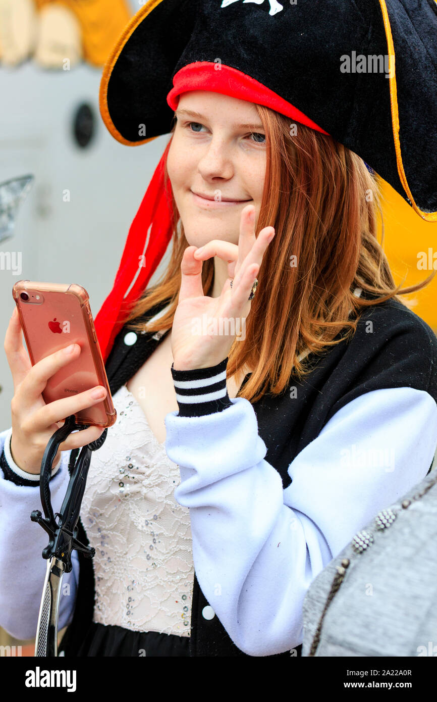 Jour pirate à Hastings. Young Caucasian woman smiling, et donner l'ok geste comme elle regarde quelqu'un d'invisible, et est titulaire d'I Phone dans la main. Close up. Banque D'Images