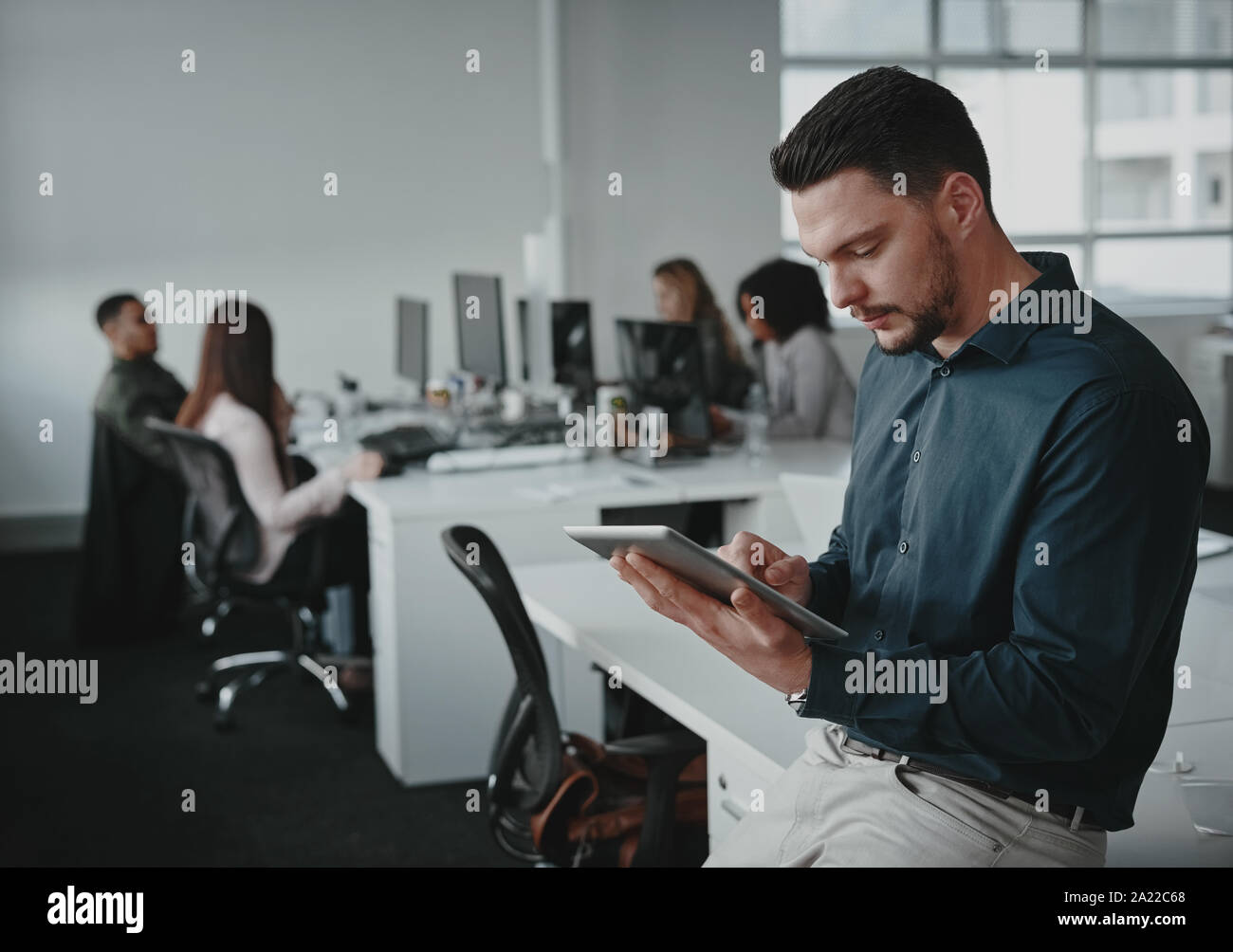 Portrait of young businessman leaning on desk using tablet pc et ses collègues travaillant dans l'arrière-plan Banque D'Images