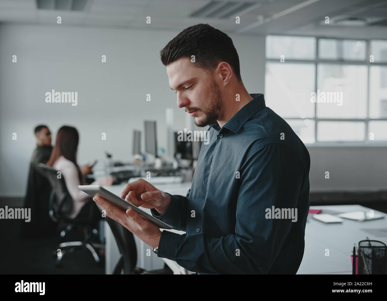 Portrait of young businessman using digital tablet occupé tandis que son collègue travaillant en arrière-plan à l'office moderne Banque D'Images