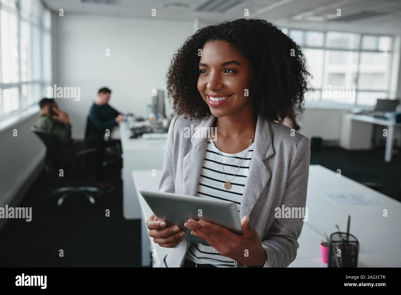 Portrait d'une jeune femme noire réussie holding digital tablet in hand looking away at office Banque D'Images