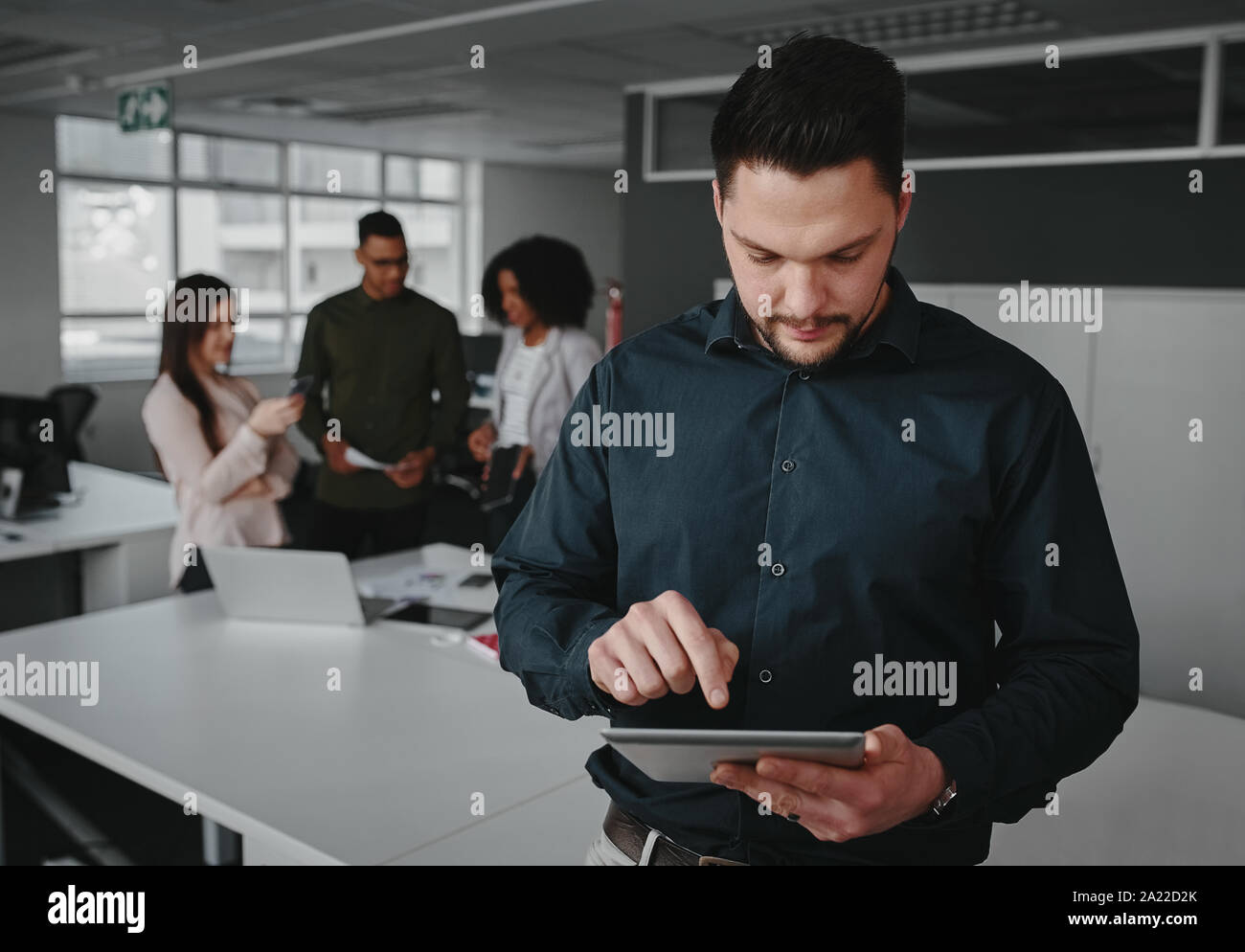 Young businessman using digital tablet tandis que ses collègues ayant discussion sur le projet dans l'arrière-plan Banque D'Images