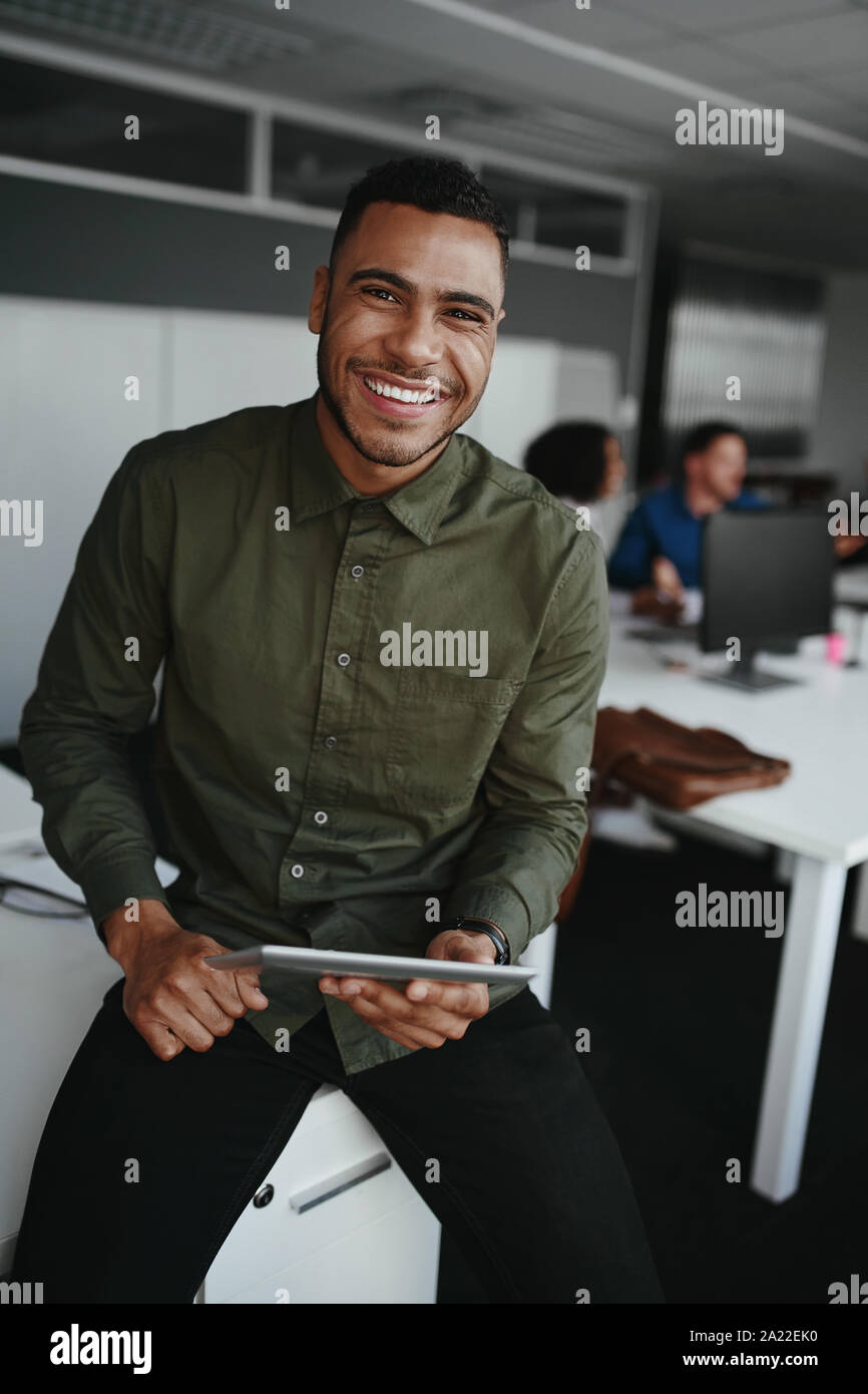 Portrait of a smiling young woman holding digital tablet in part à la recherche d'appareil photo et collègue au contexte Banque D'Images