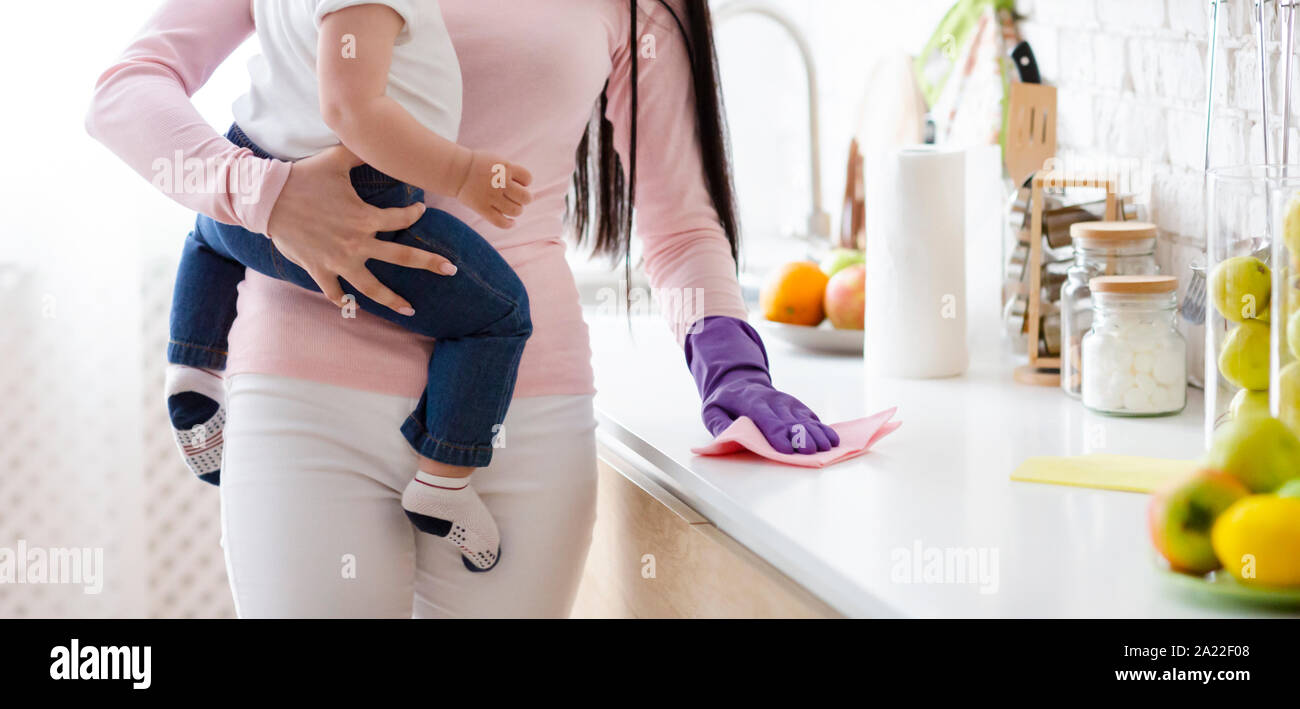 La vie domestique. Mother holding baby et le nettoyage de la table de cuisine, panorama avec l'espace vide Banque D'Images