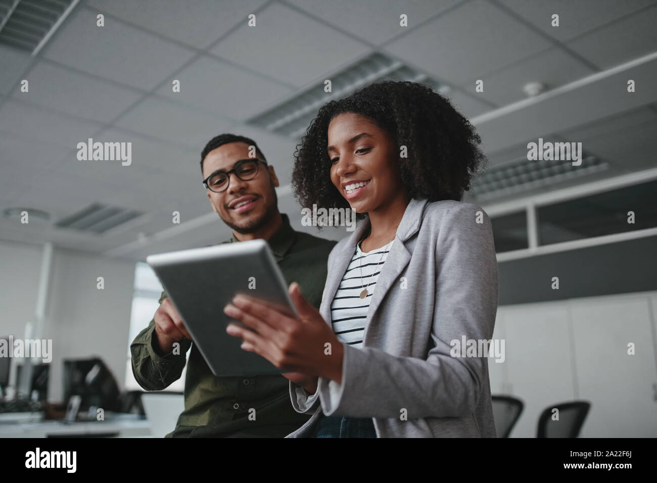 Portrait of smiling professional young African American businesswoman showing données sur tablette numérique à homme in office Banque D'Images