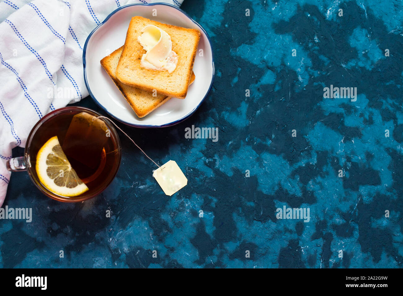 Grille-pain avec du beurre et du thé avec des citrons sur un fond bleu. Un petit-déjeuner léger. Copier l'espace. Banque D'Images