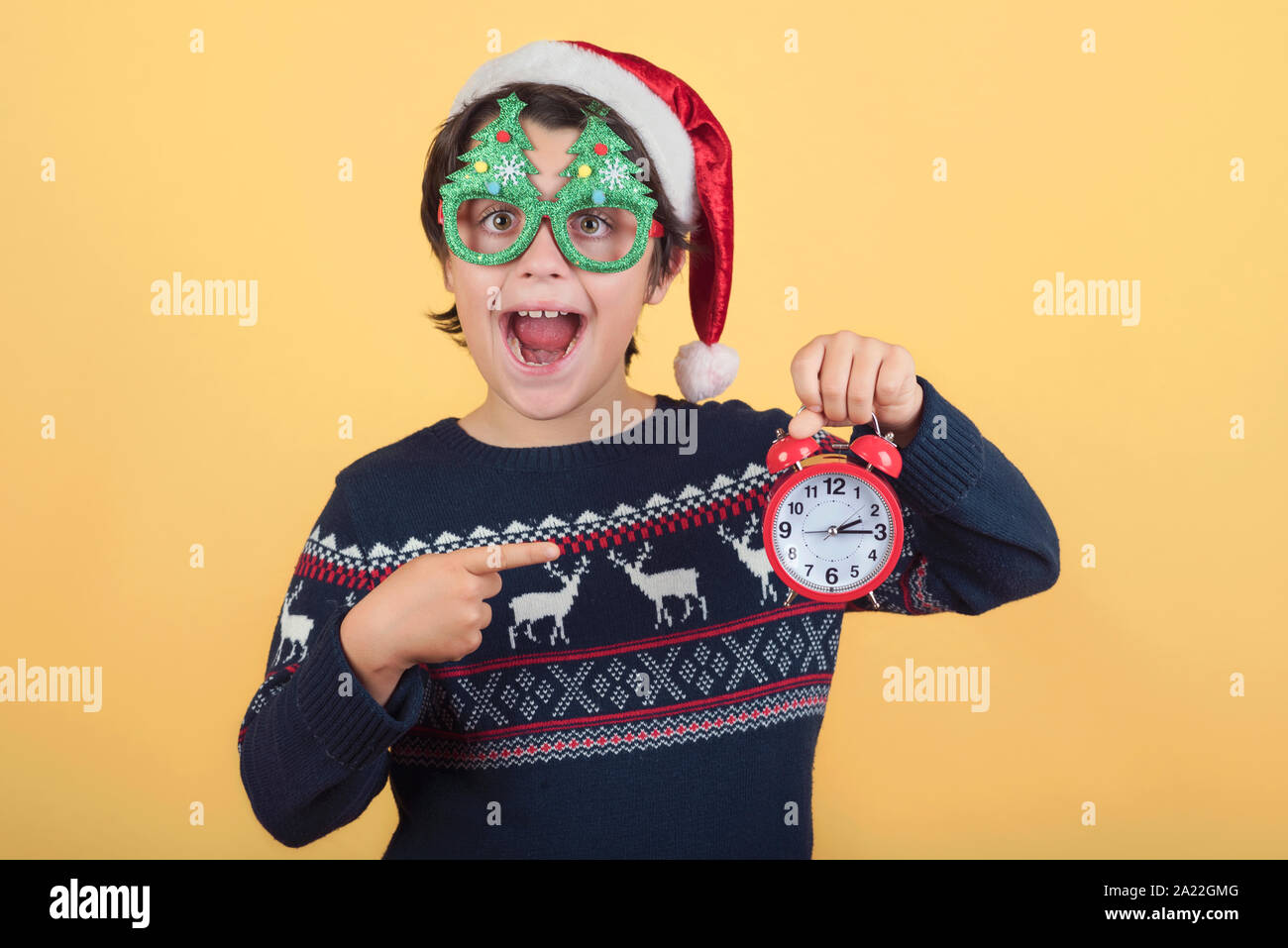 Enfant drôle avec réveil Wearing Christmas Santa Claus Hat sur fond jaune Banque D'Images