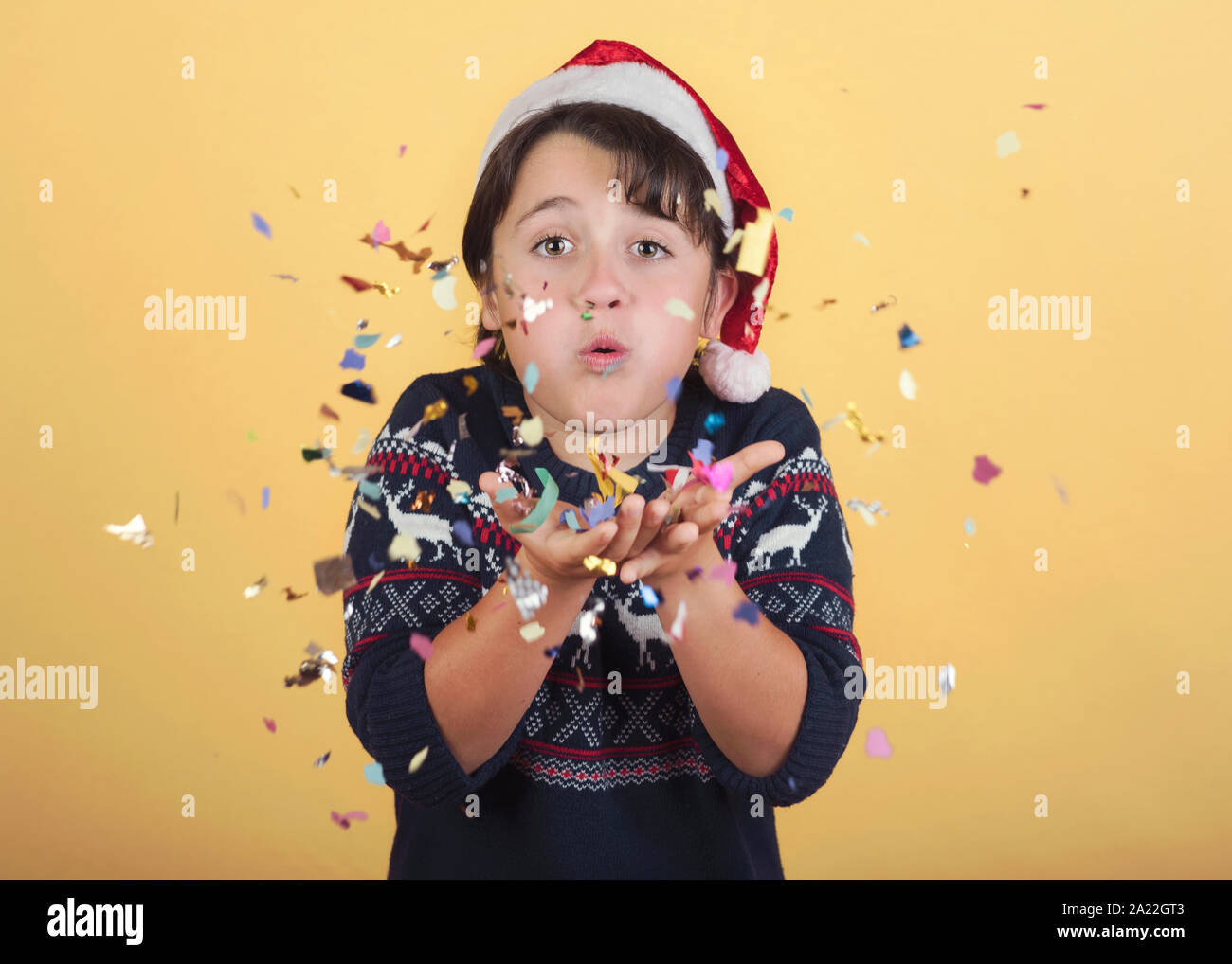 Soufflage enfant confetti Wearing Christmas Santa Claus Hat sur fond jaune Banque D'Images