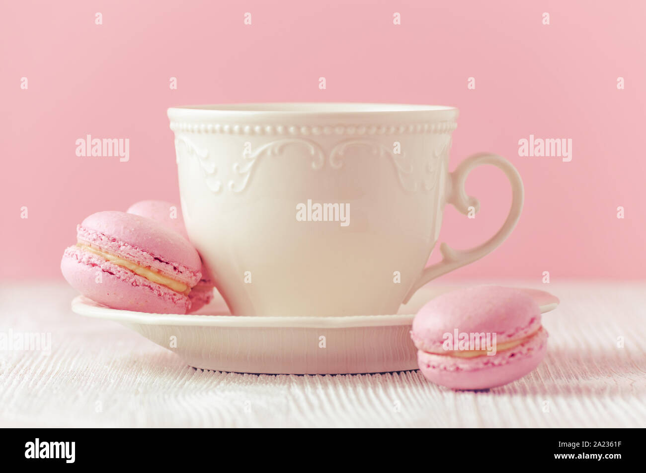 Macarons rose avec à la main une tasse de café sur fond rose tonique, selective focus Banque D'Images