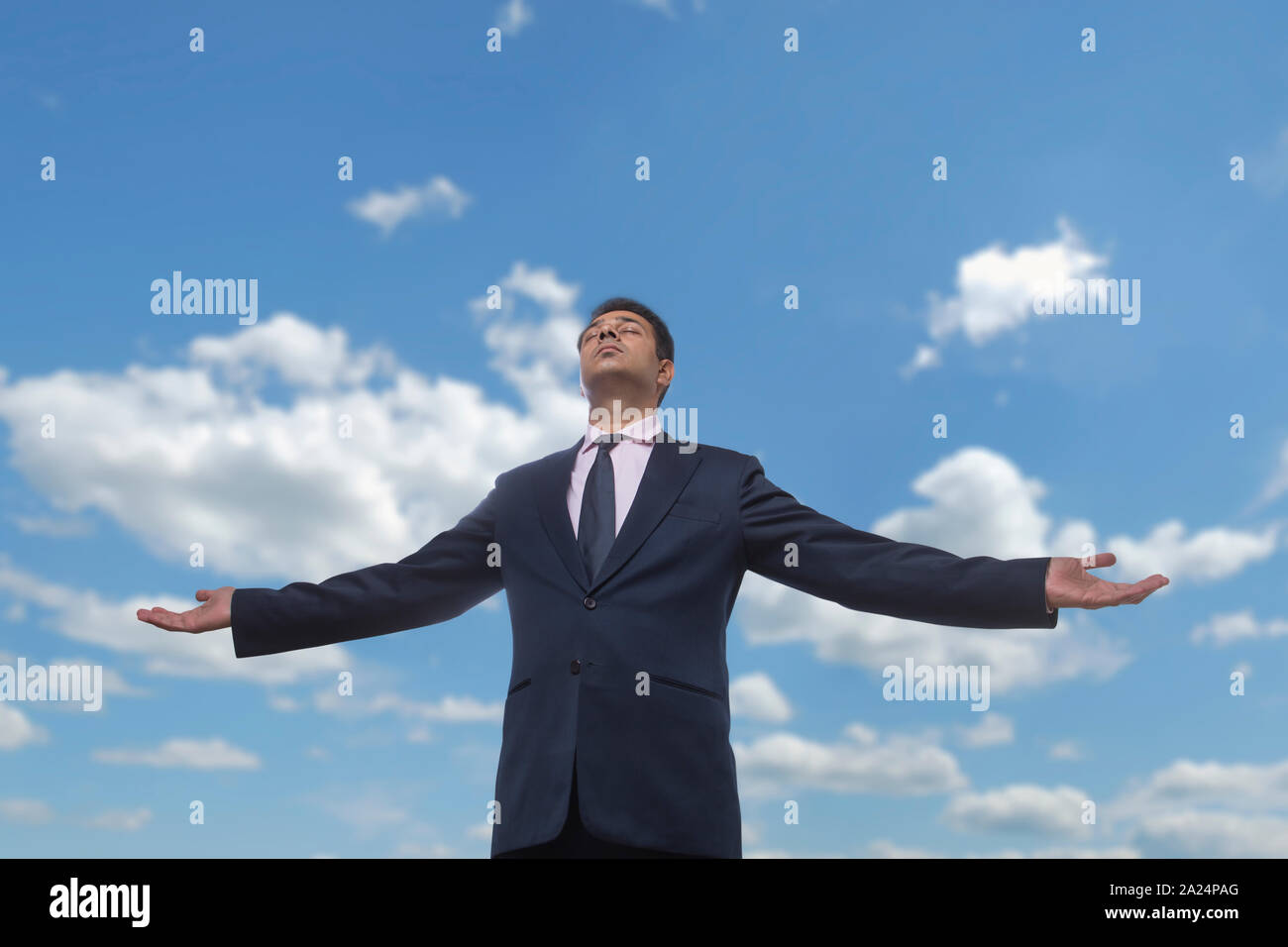 Homme d'affaires de vêtements formels debout avec les bras ouverts et les yeux fermés contre un ciel nuageux ciel bleu Banque D'Images