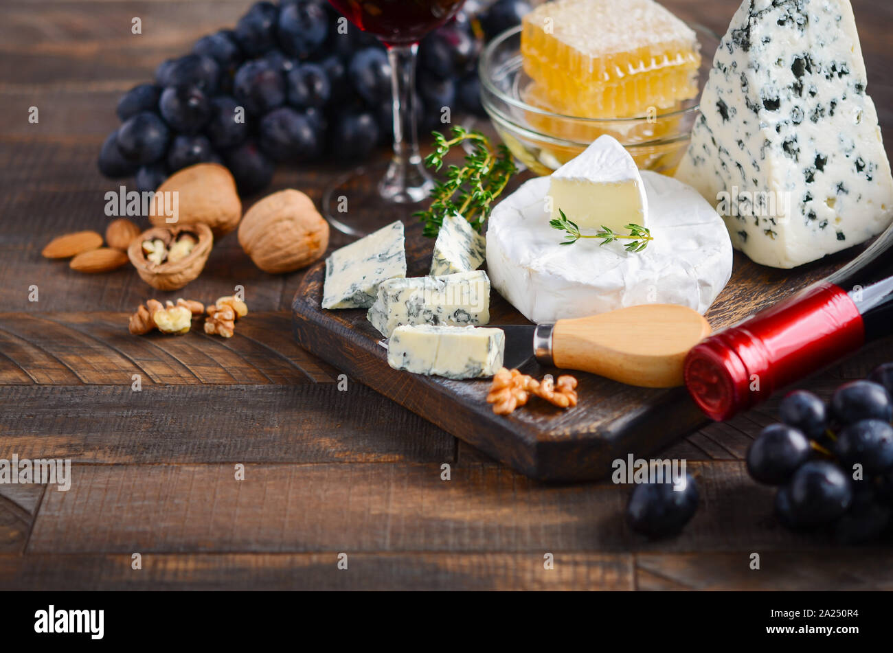 Assiette de fromage aux raisins, miel, noix et vin rouge sur une table en bois. Banque D'Images