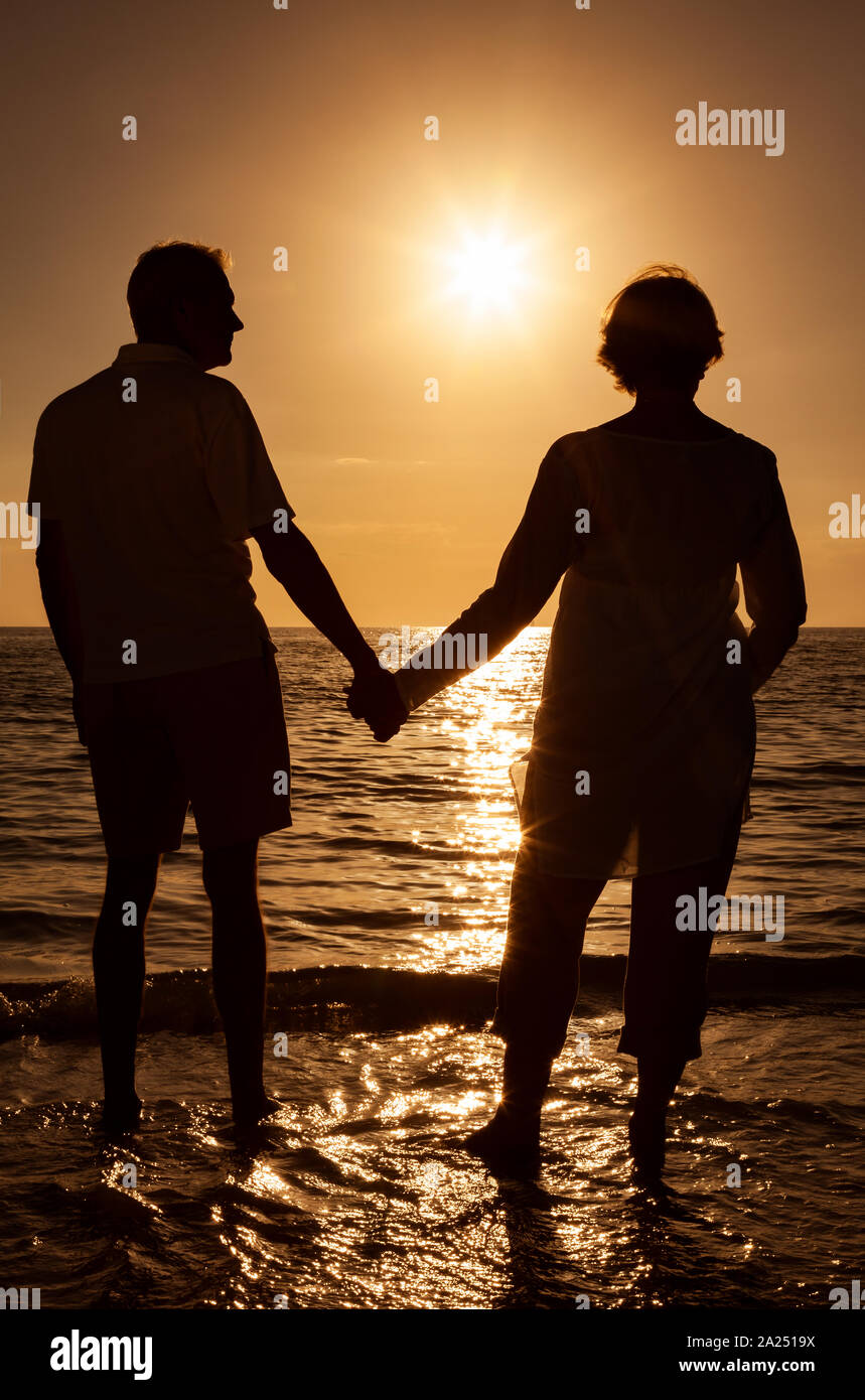 L'homme et la femme Senior couple holding hands au coucher et au lever du soleil sur une plage tropicale déserte Banque D'Images
