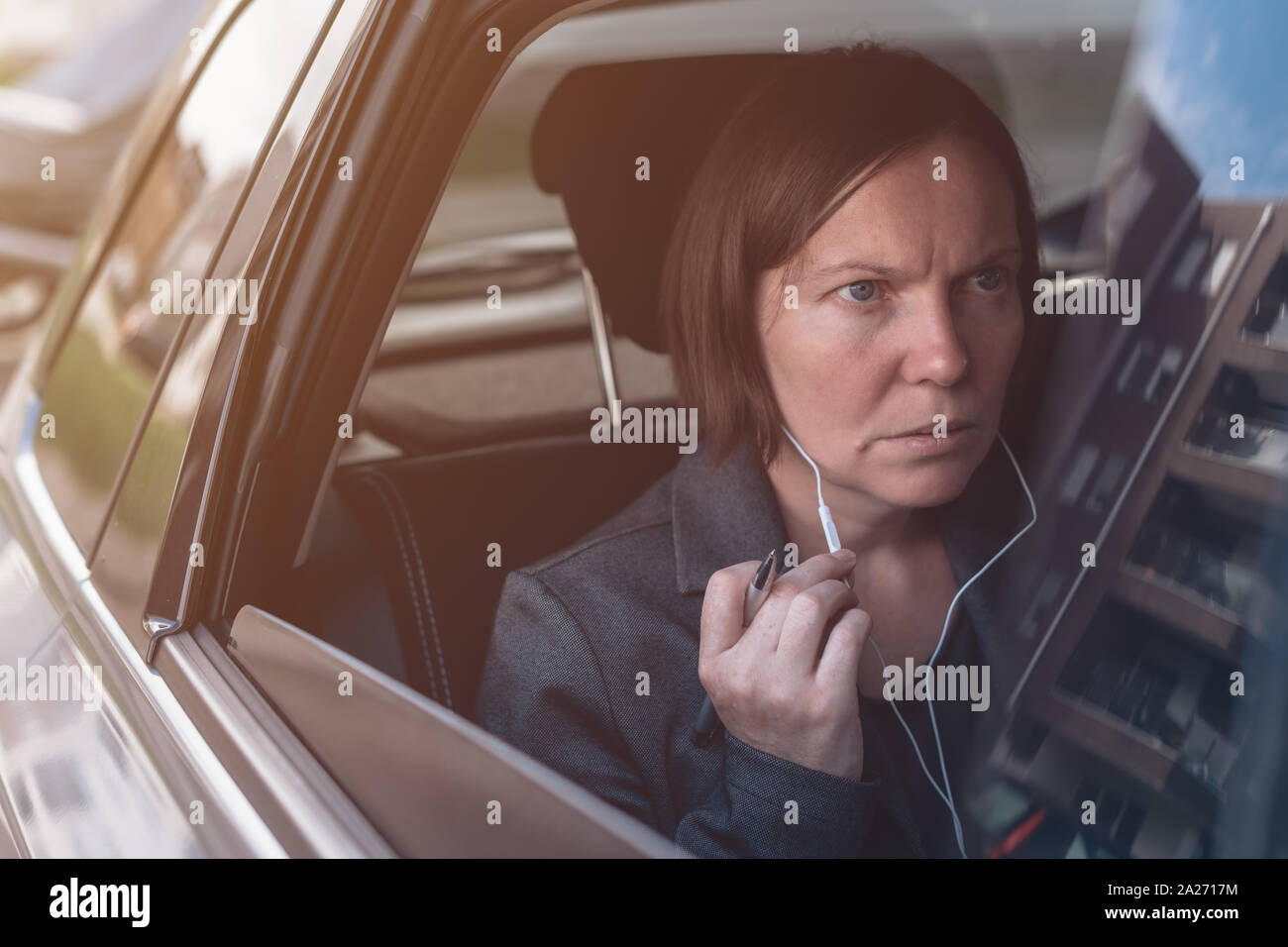 Businesswoman dictée dans microphone écouteurs smartphone tout en étant assis à l'arrière siège de voiture de société Banque D'Images