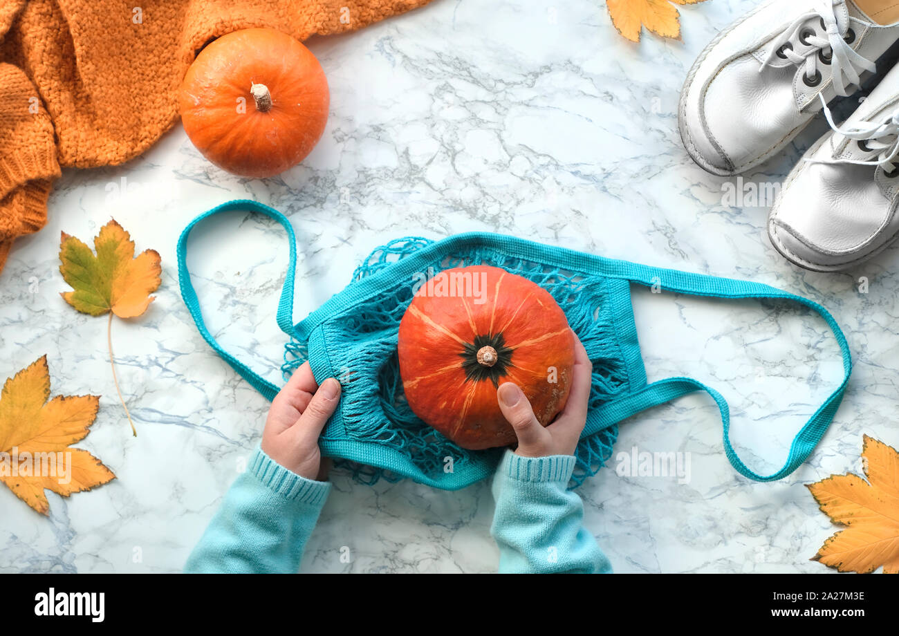 Mise à plat de l'automne avec des mains mettre orange citrouille en string  turquoise ou sac-filet. Vue de dessus sur la lumière en arrière-plan avec  des chaussures blanches, swea Photo Stock -