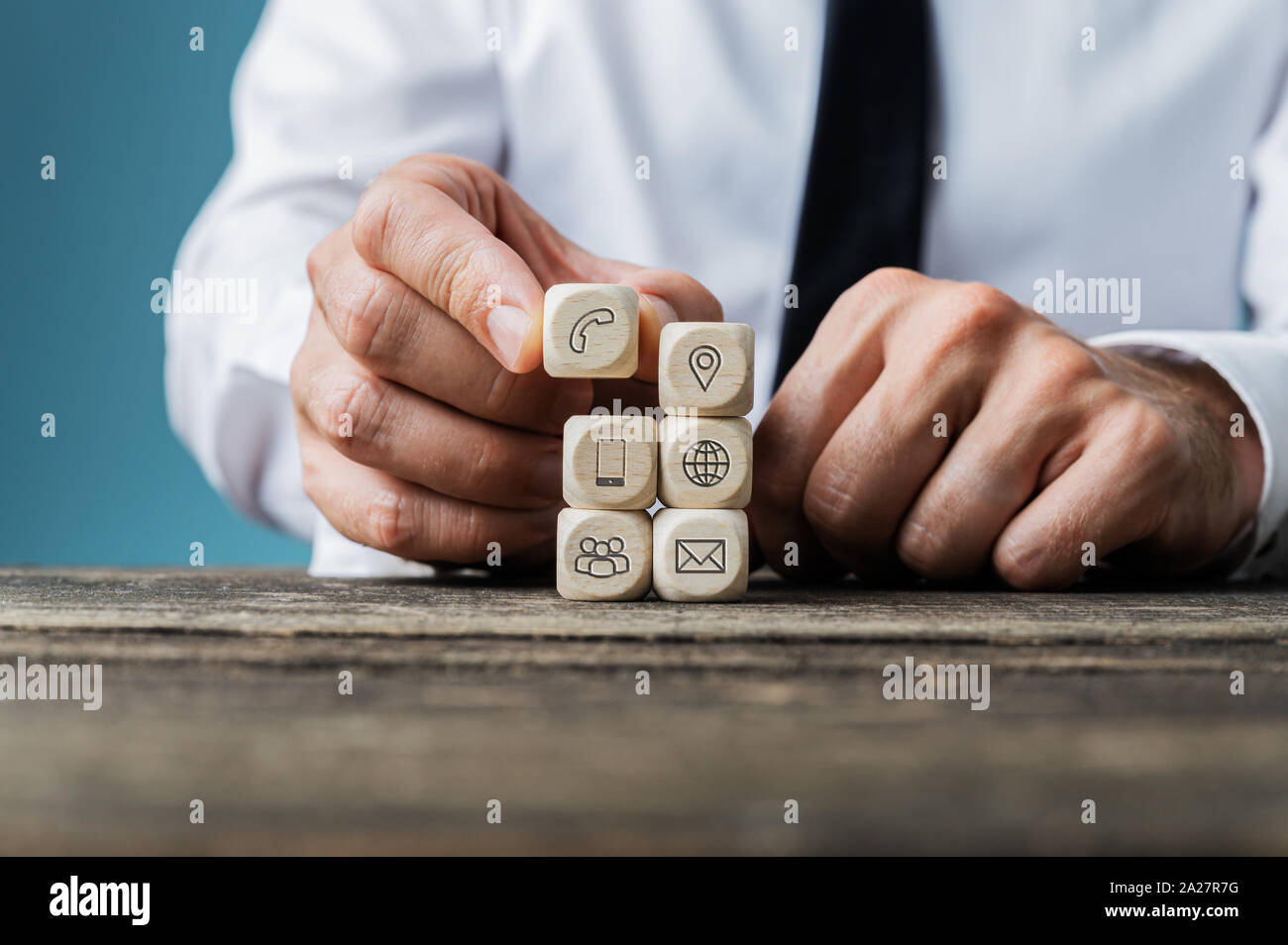 Empilage de dés en bois avec l'homme et de l'information de contact sur les icônes sur leur bureau en bois rustique. Banque D'Images