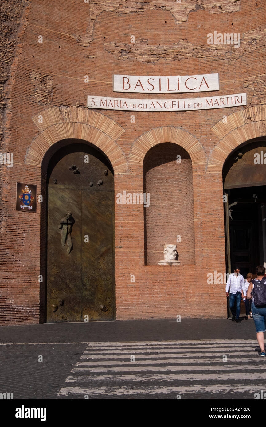 Comparaison de deux arches d'entrée avec grande les portes métalliques de l'église Santa Maria deli Angeli montrant des têtes 3D et le Christ avec croix à travers lui. Banque D'Images